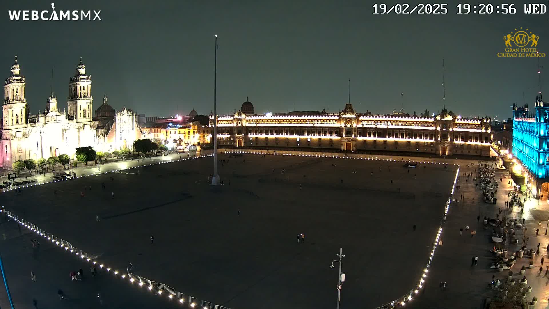 A large, brightly lit plaza at night is shown, with a cathedral and government buildings visible in the background under a dark sky.
