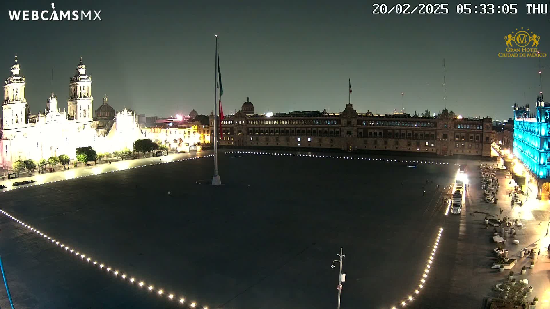 A nighttime, aerial view of a large plaza with a cathedral and government buildings illuminated, under a dark sky.