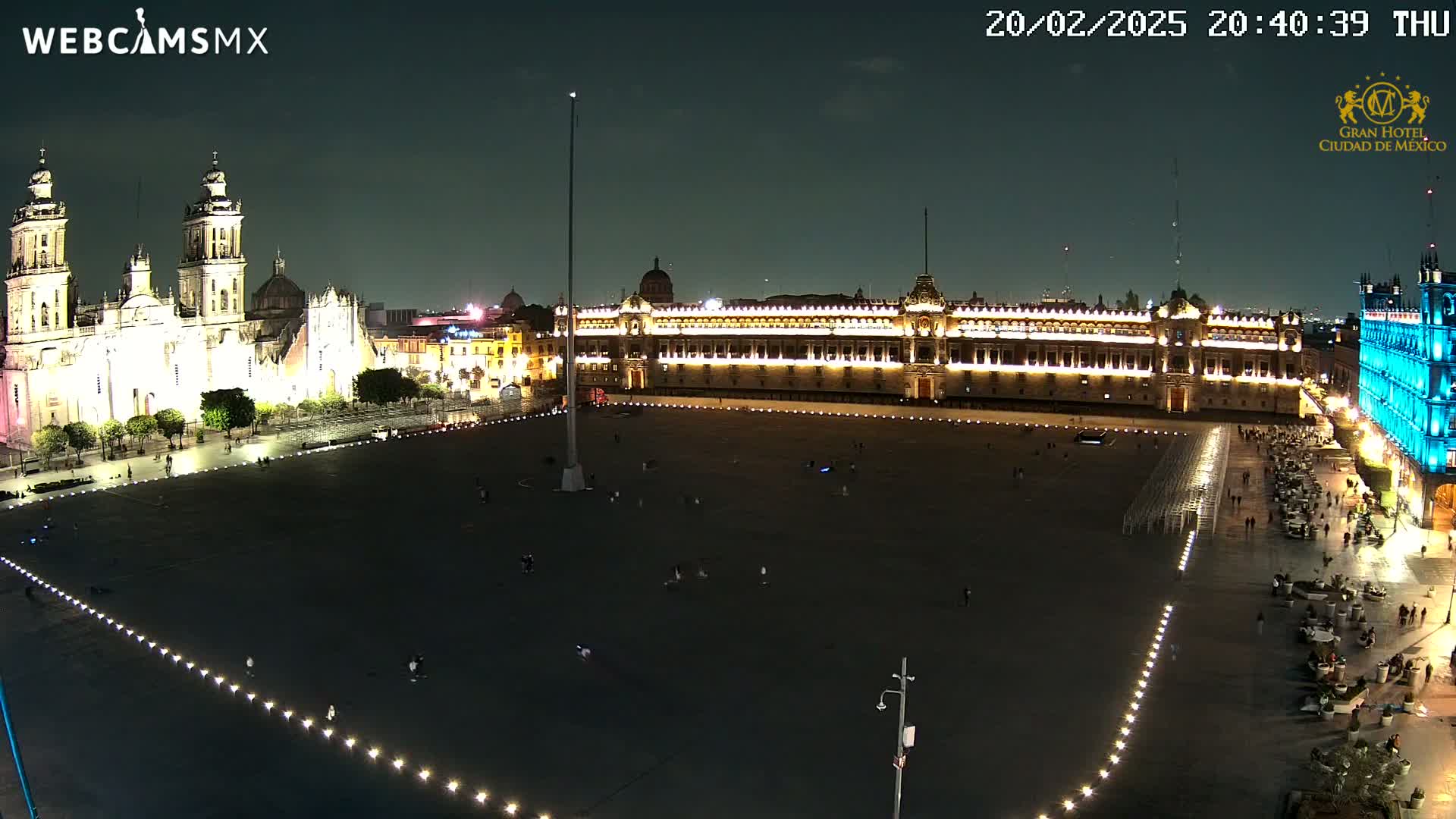 A large, mostly empty plaza at night is illuminated, flanked by a brightly lit cathedral and palace.