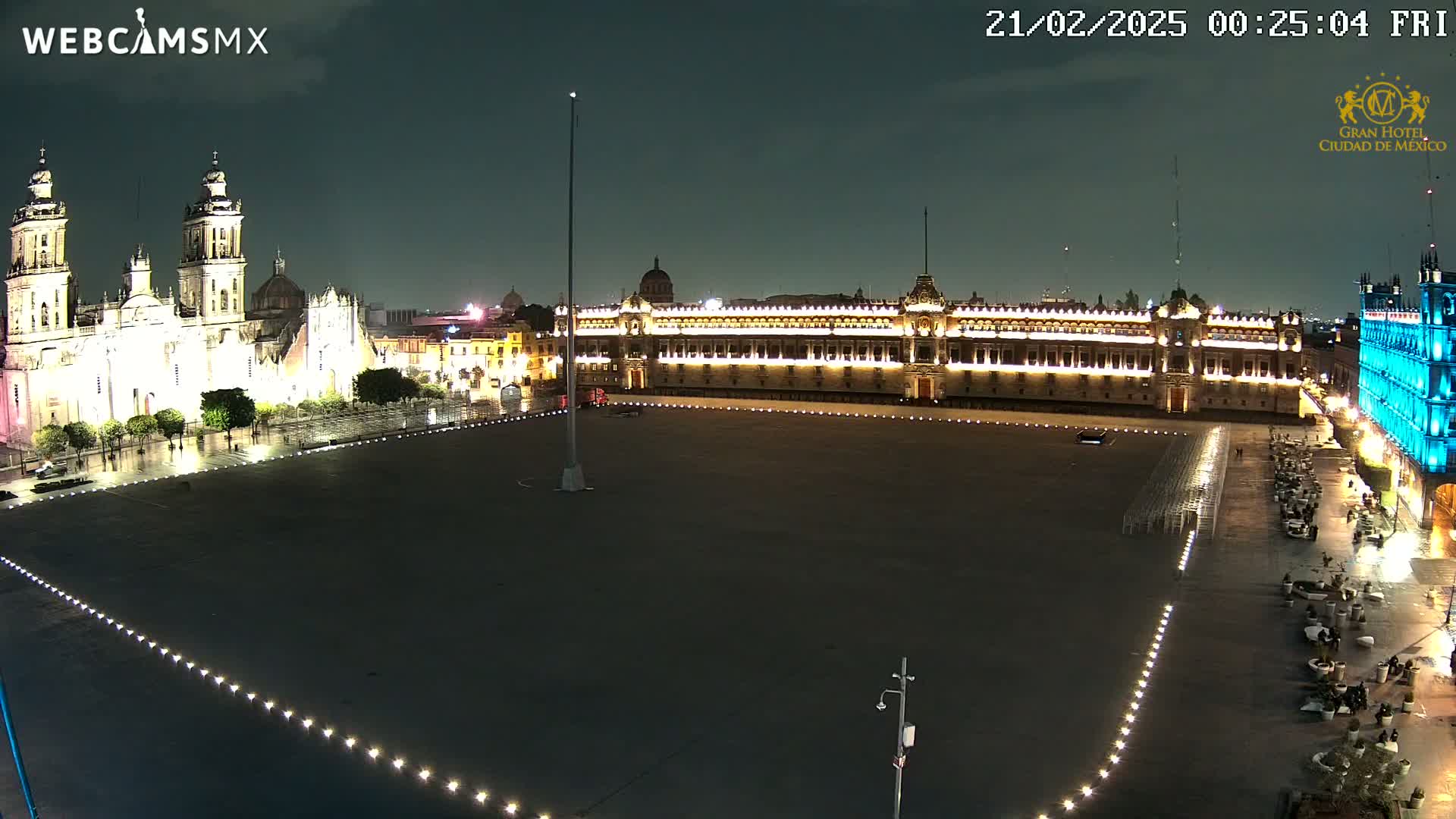 A large, empty plaza at night is illuminated, with a cathedral and government building visible in the background under a dark sky.