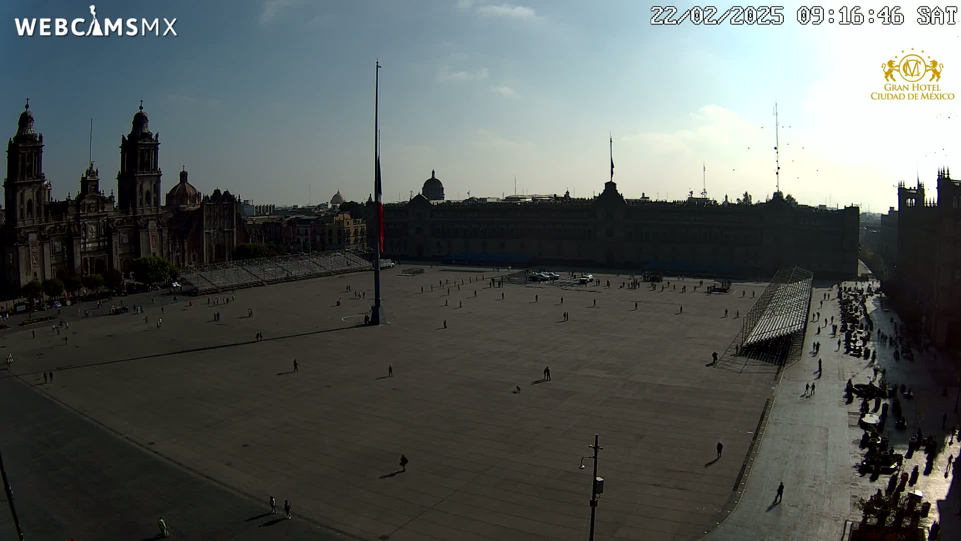 A large plaza with a cathedral and government building in the background, under a mostly clear sky, is sparsely populated with people.
