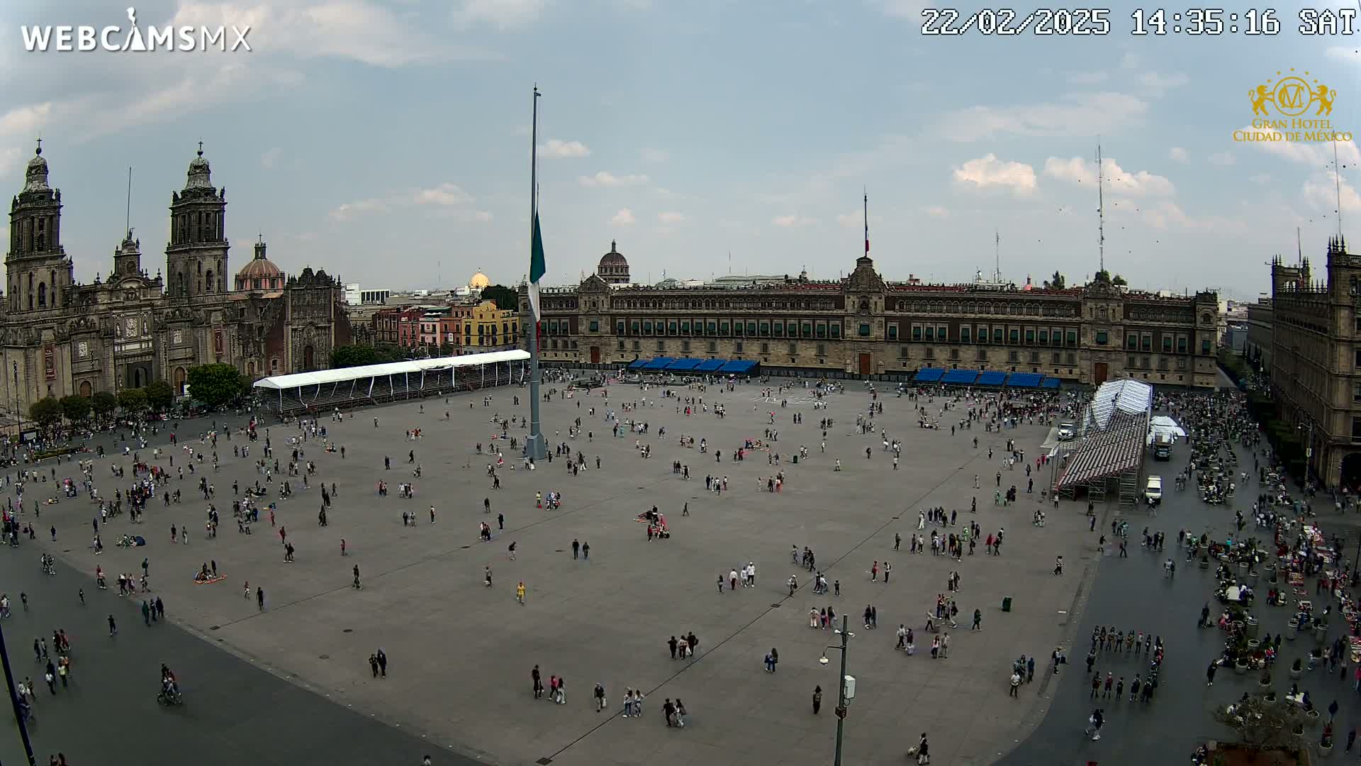 A large plaza with many people, a cathedral, and a government building is seen on a partly cloudy day.