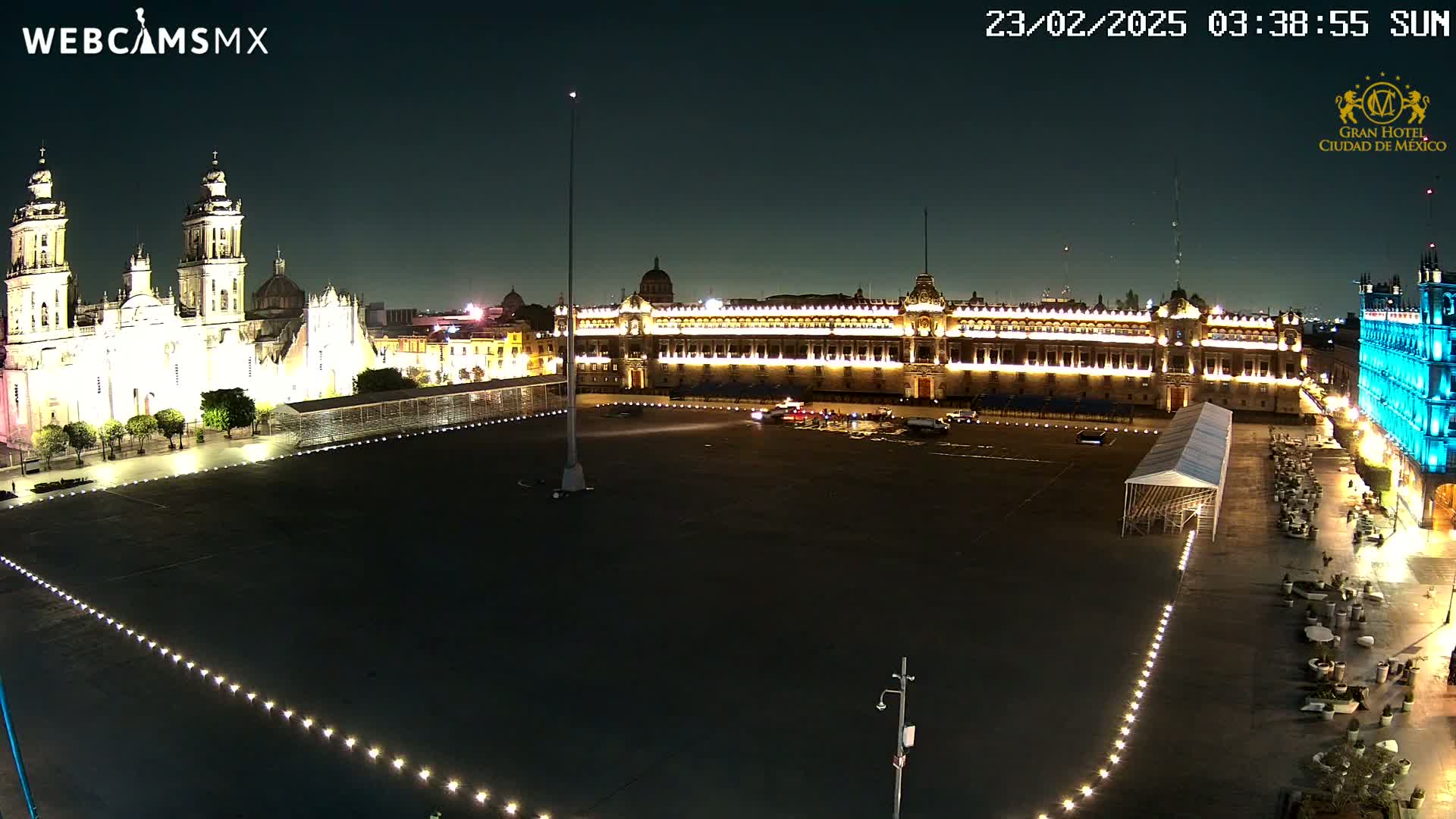 A large, mostly empty plaza at night is illuminated, with a brightly lit cathedral and palace visible in the background under a clear, dark sky.