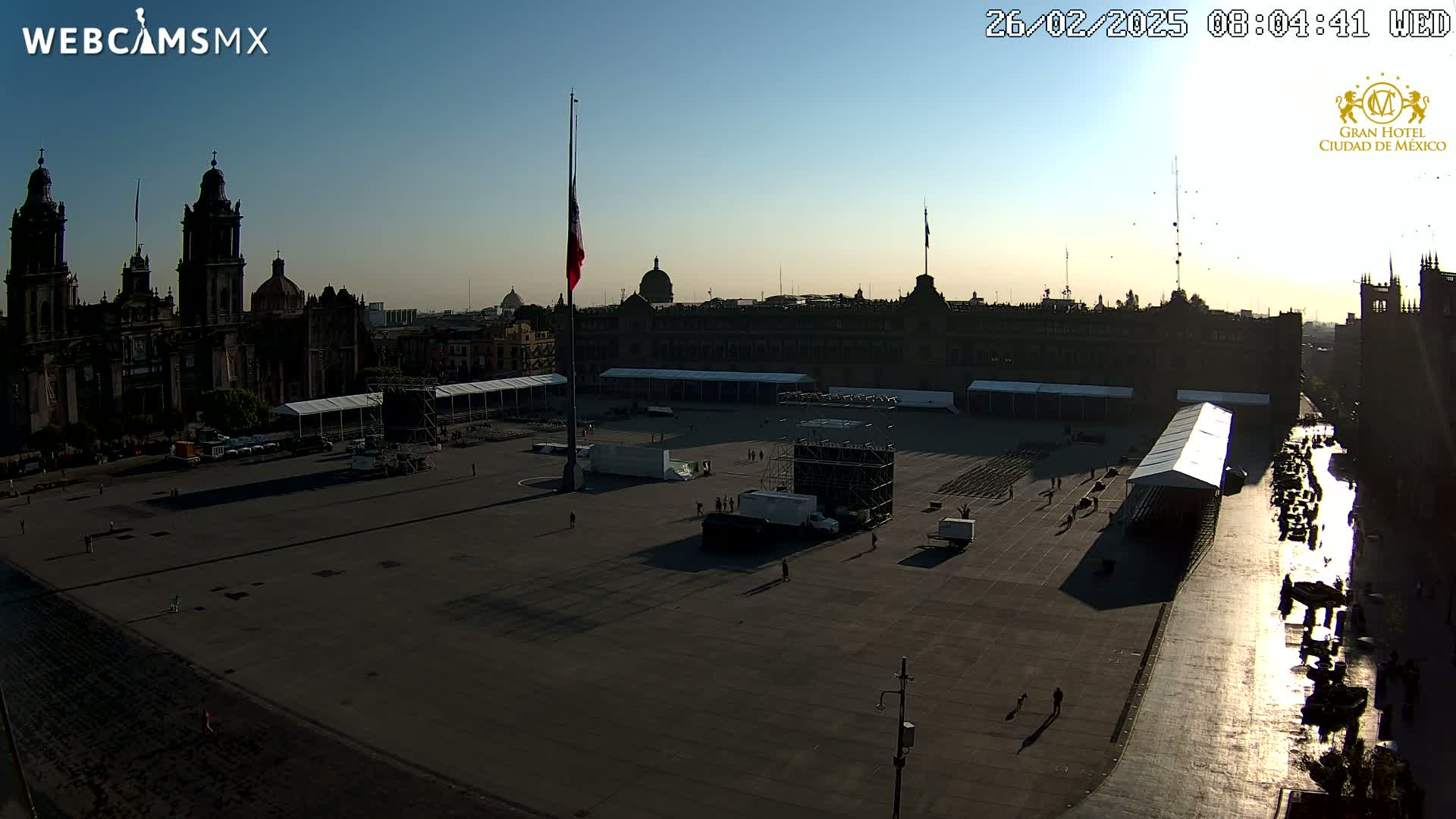 A large plaza in front of a cathedral and government building is being prepped for an event under a clear, bright morning sky.