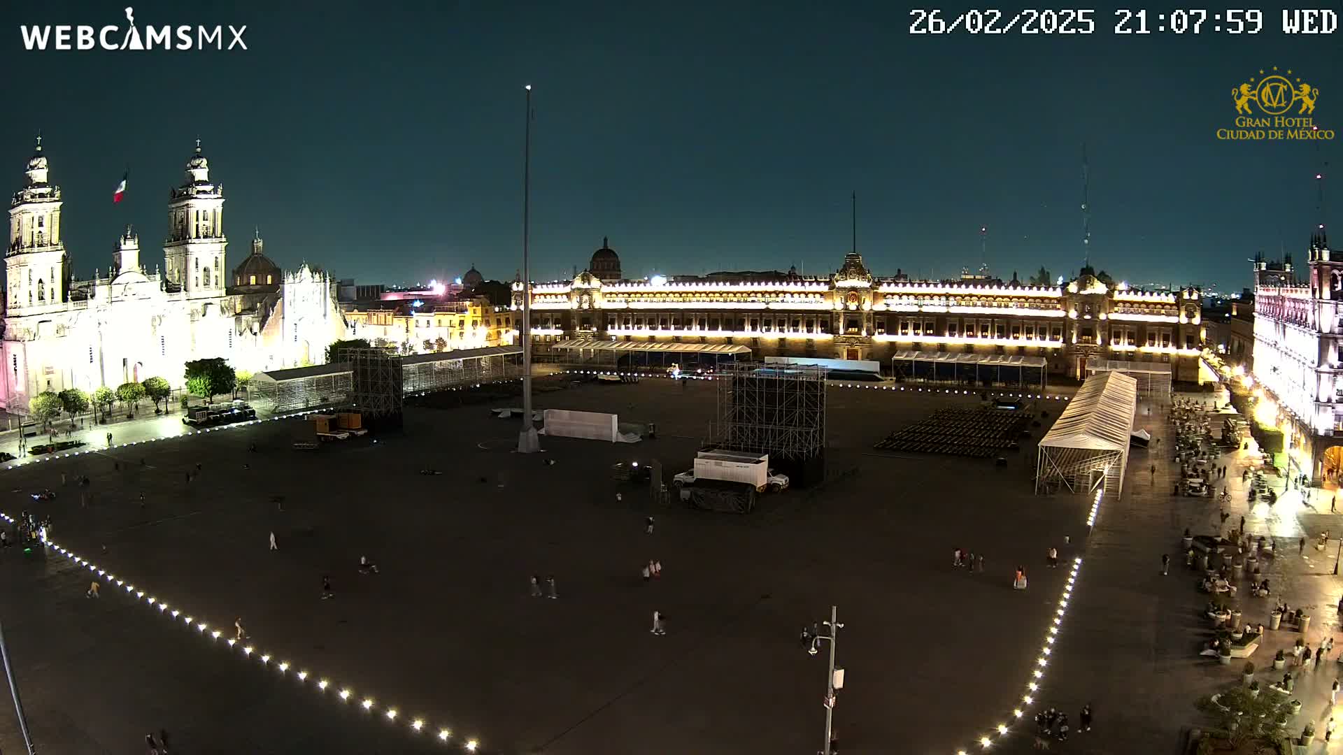 A nighttime, aerial view of a large, mostly empty plaza with a cathedral and government building illuminated, under a clear sky.