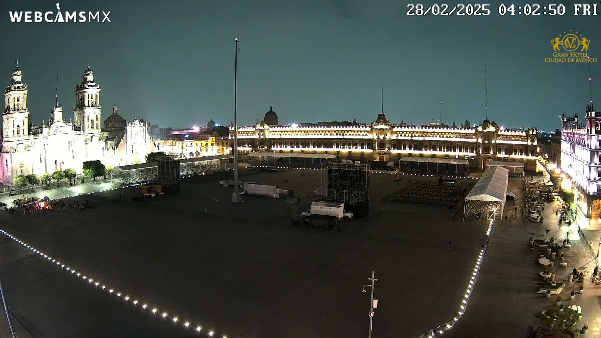 A large, mostly empty plaza at night, flanked by illuminated buildings including a cathedral and a palace, under a dark sky.