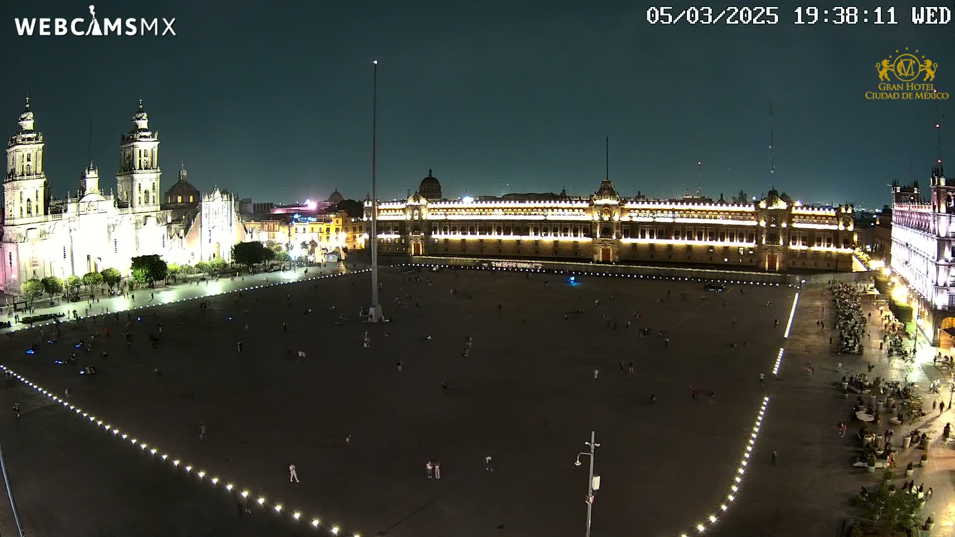 A large, mostly empty plaza at night is illuminated, with a brightly lit cathedral and palace visible in the background under a clear, dark sky.