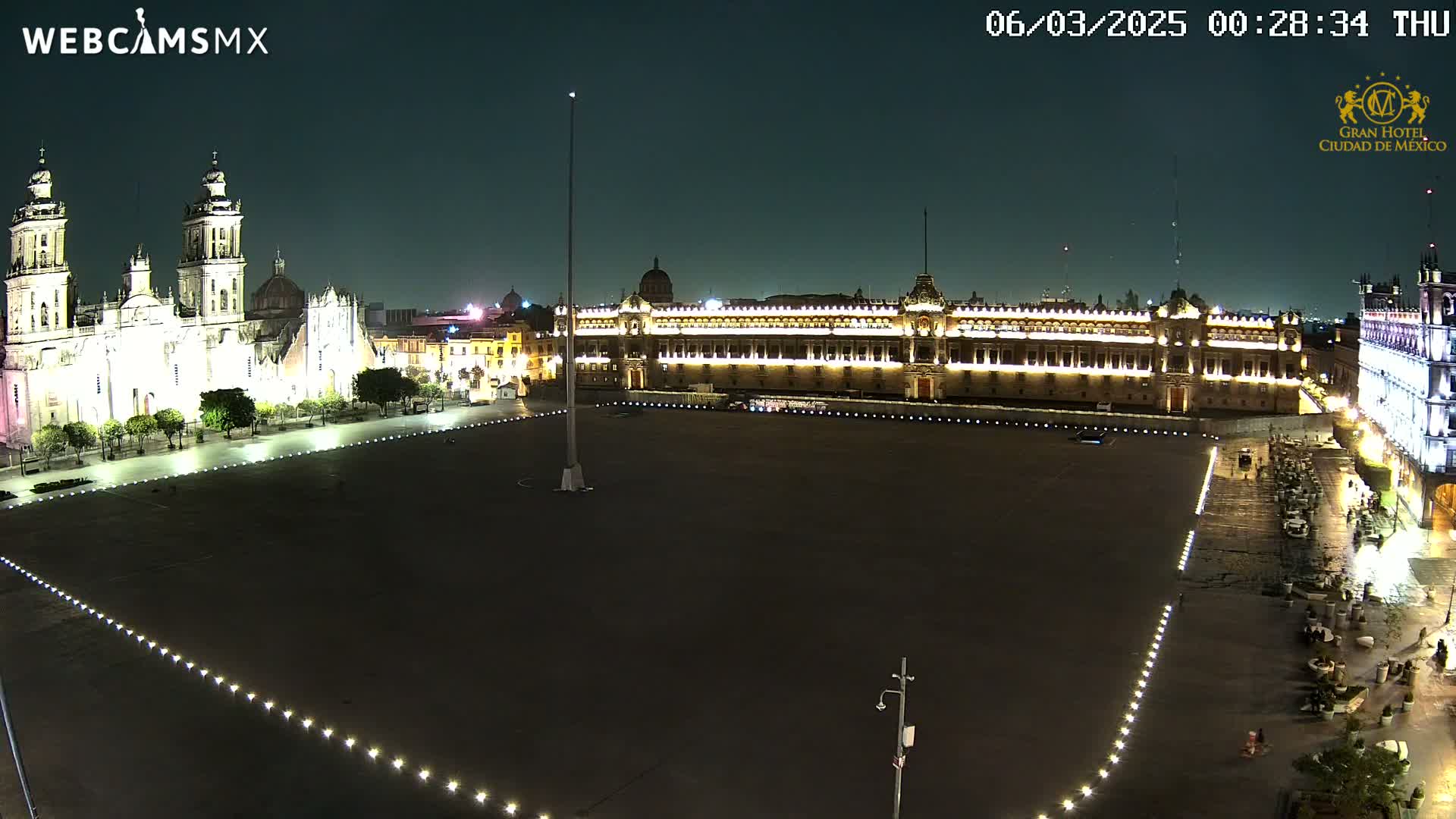 A large, mostly empty plaza at night, bordered by illuminated historical buildings, under a dark sky.