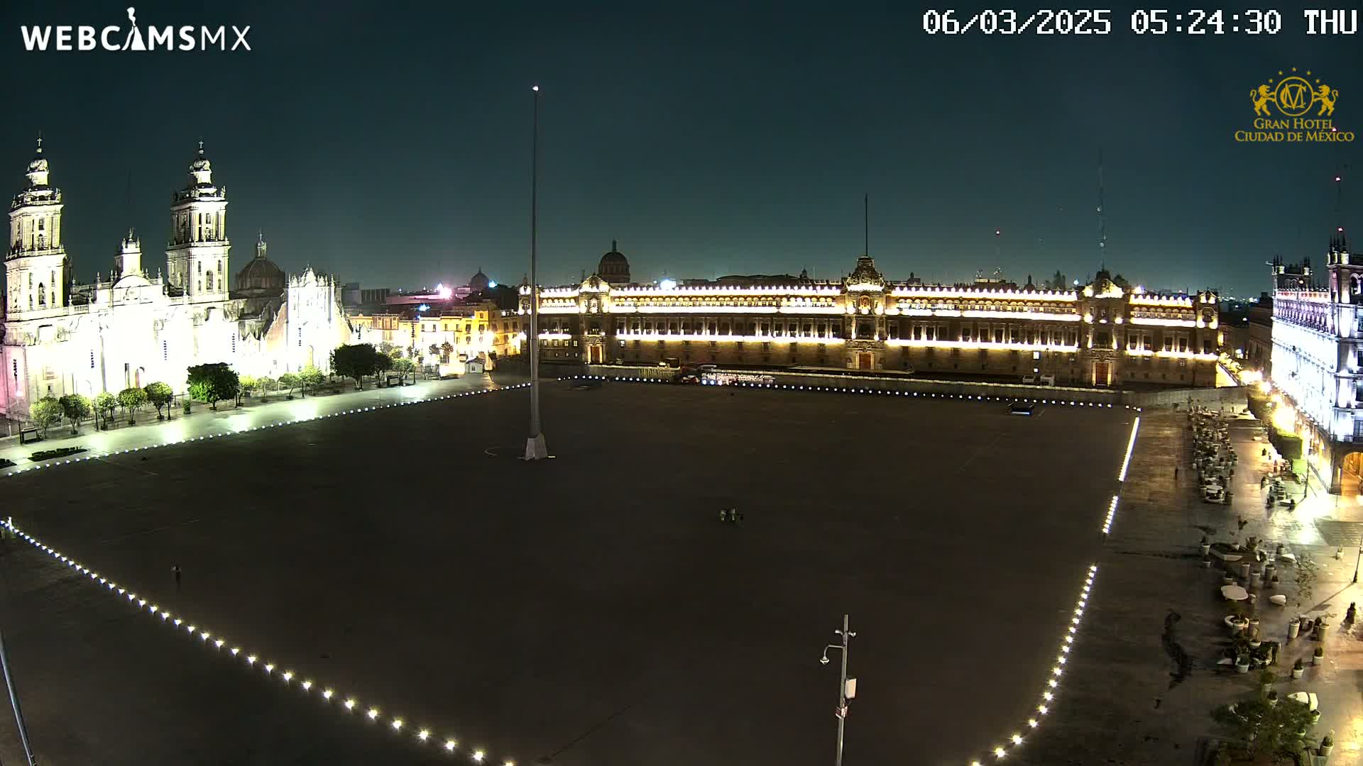 A large, mostly empty plaza at night is illuminated, with a cathedral and government building visible on either side.