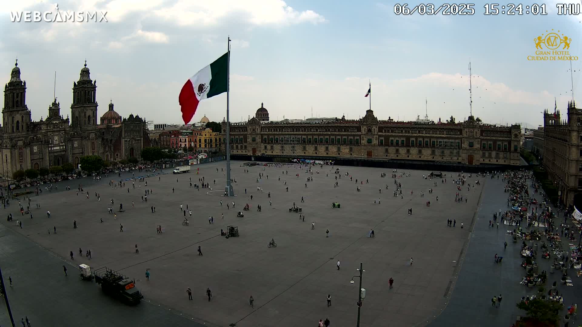 A large plaza with a few people scattered across it, overlooked by a grand building and cathedral, under a partly cloudy sky.