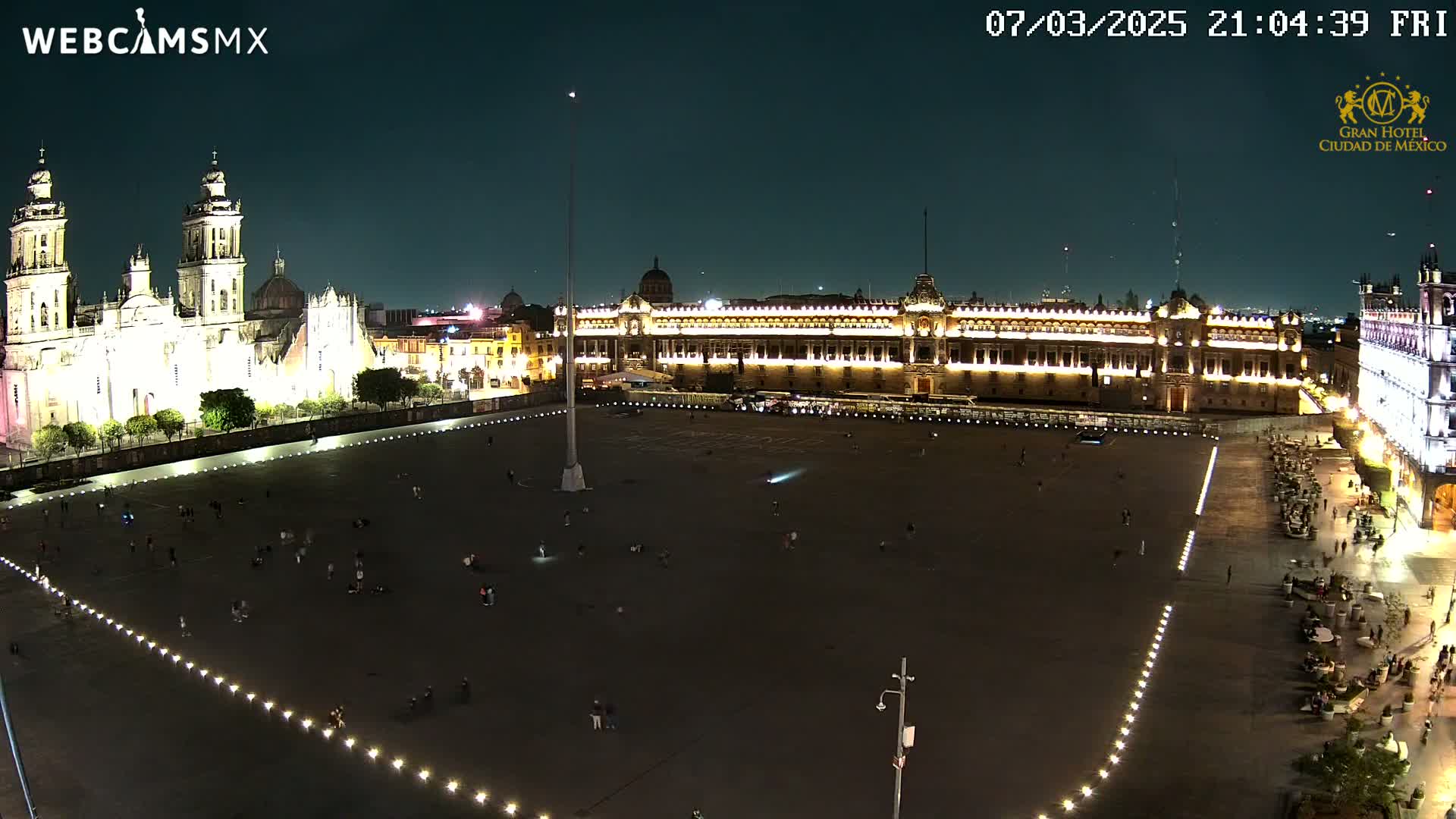 A large, mostly empty plaza at night, illuminated by lights, is surrounded by brightly lit historical buildings under a dark sky.