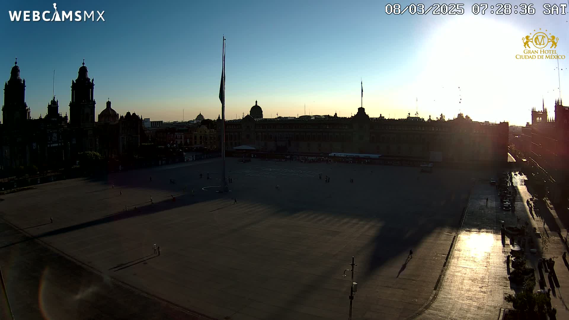 A large plaza at sunrise is surrounded by historic buildings, with long shadows cast across the mostly empty space.