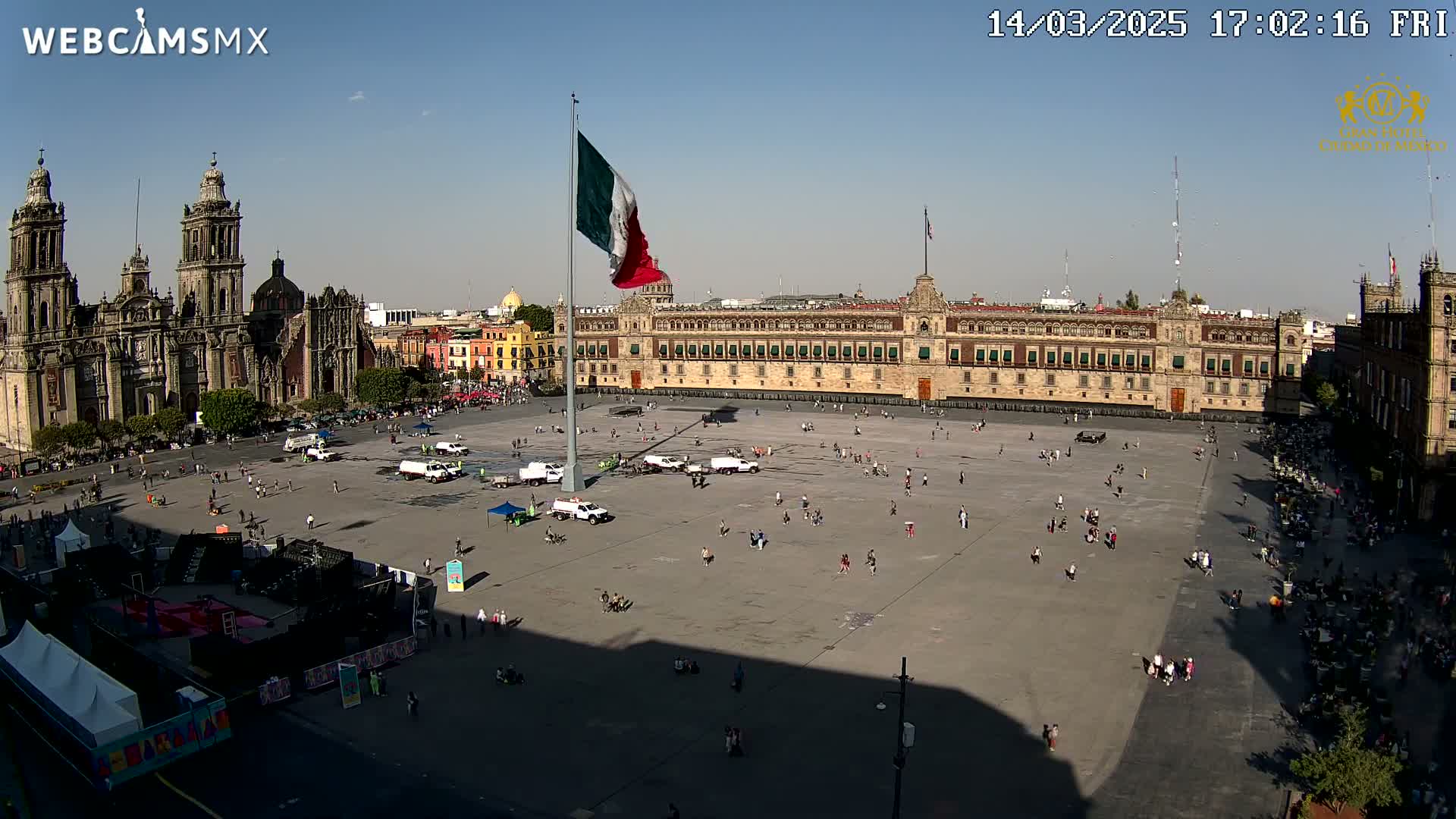 A large plaza with a cathedral and government building is shown on a sunny day, with a few people scattered throughout the square.