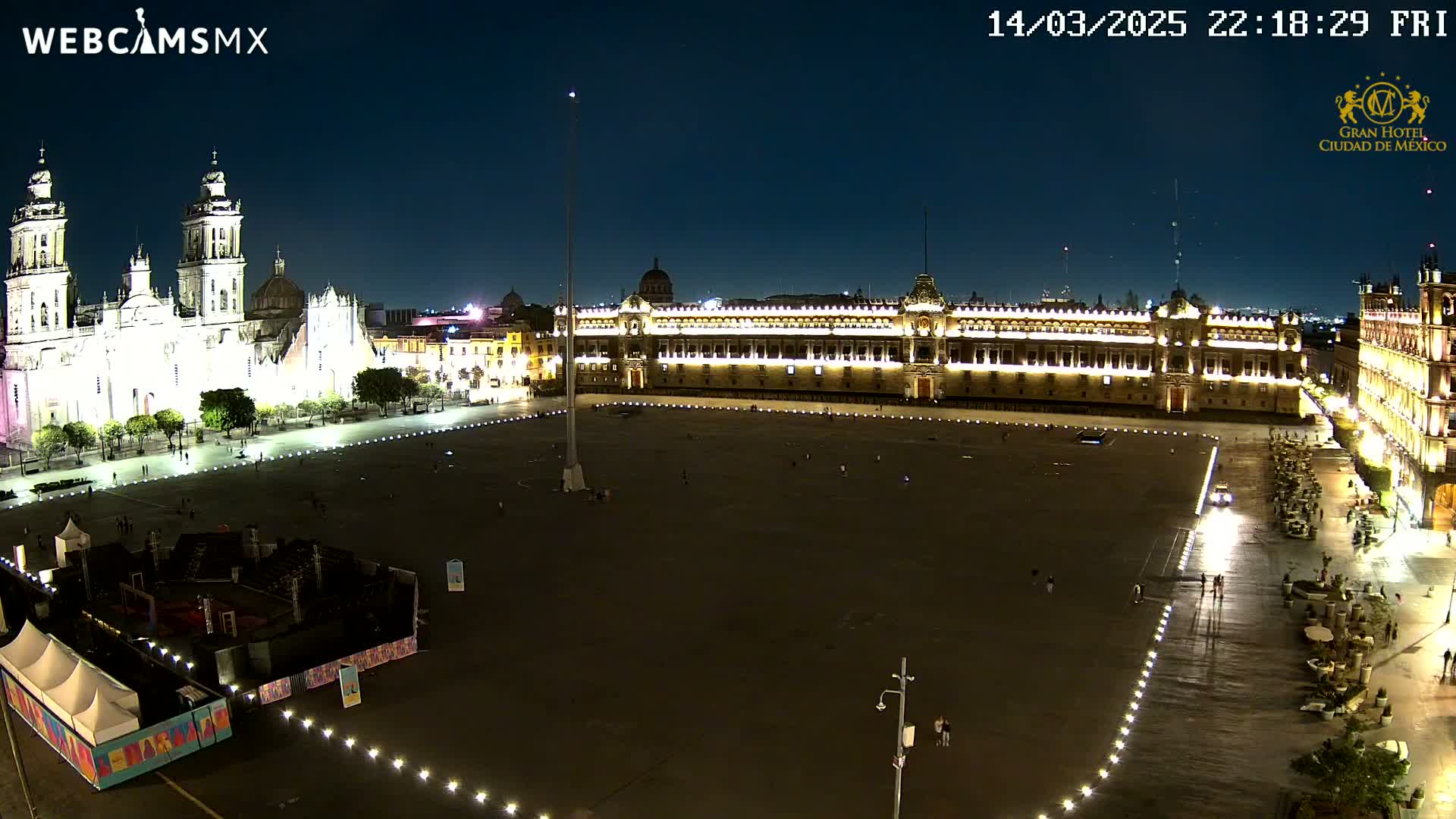 A large, mostly empty plaza at night, flanked by illuminated historical buildings, including a cathedral and a palace.