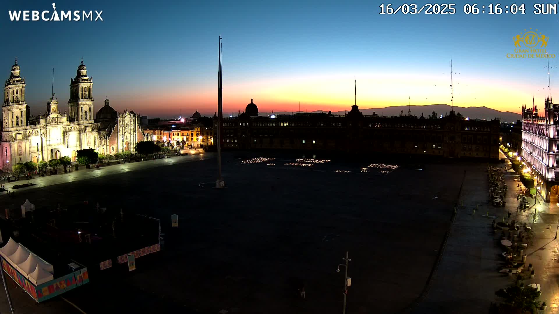A large plaza at twilight, with a brightly lit cathedral on one side and other buildings illuminated against a colorful sunset sky.