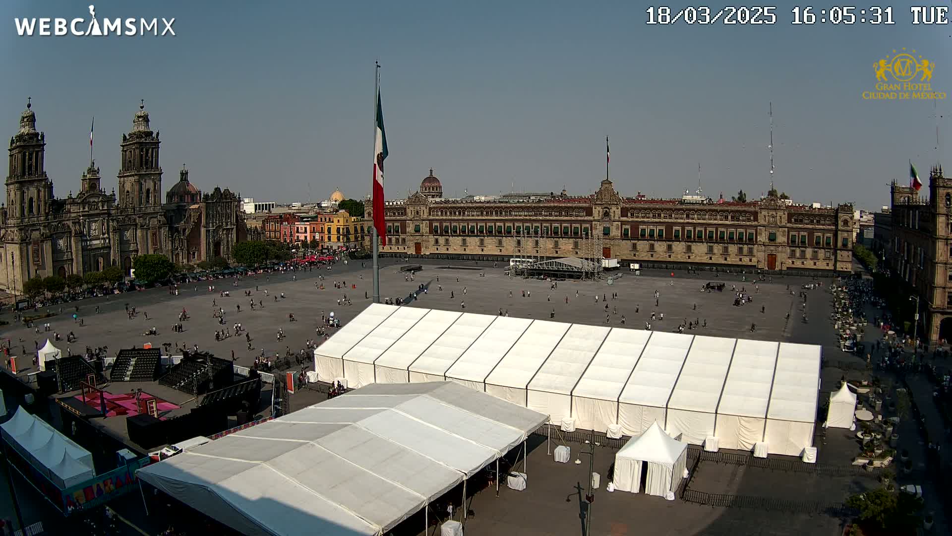 A large plaza with several tents, a cathedral, and a long government building is visible under a sunny sky.