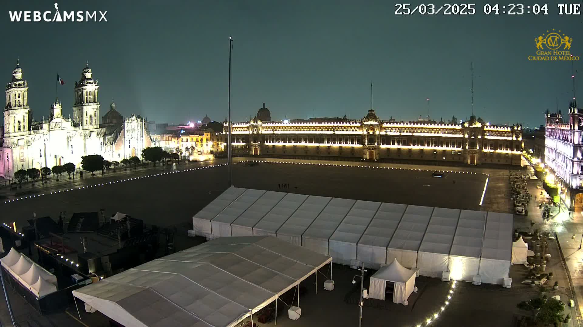 A nighttime view of a large plaza with a cathedral and government building illuminated, surrounded by several large white tents under a dark, possibly overcast sky.