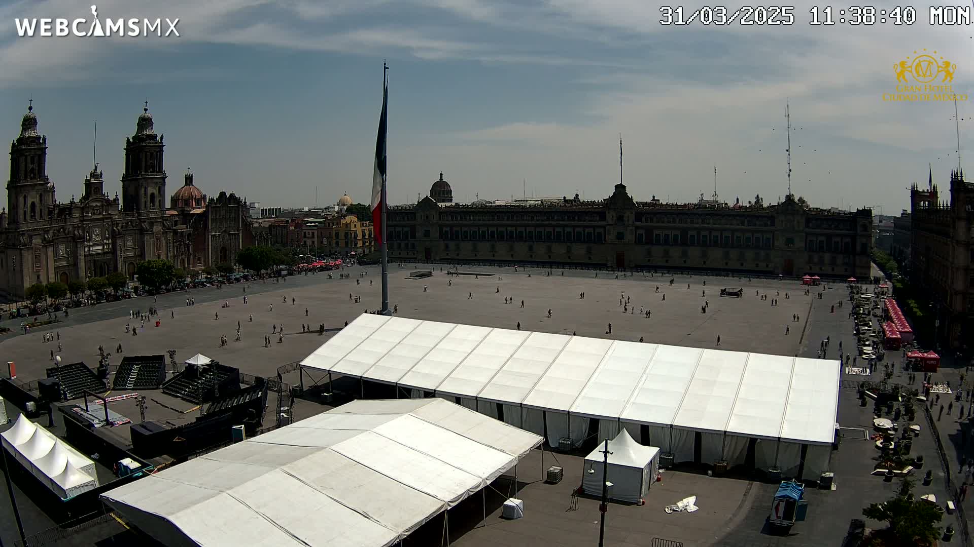 A large plaza with several white tents, surrounded by historical buildings under a mostly sunny sky.