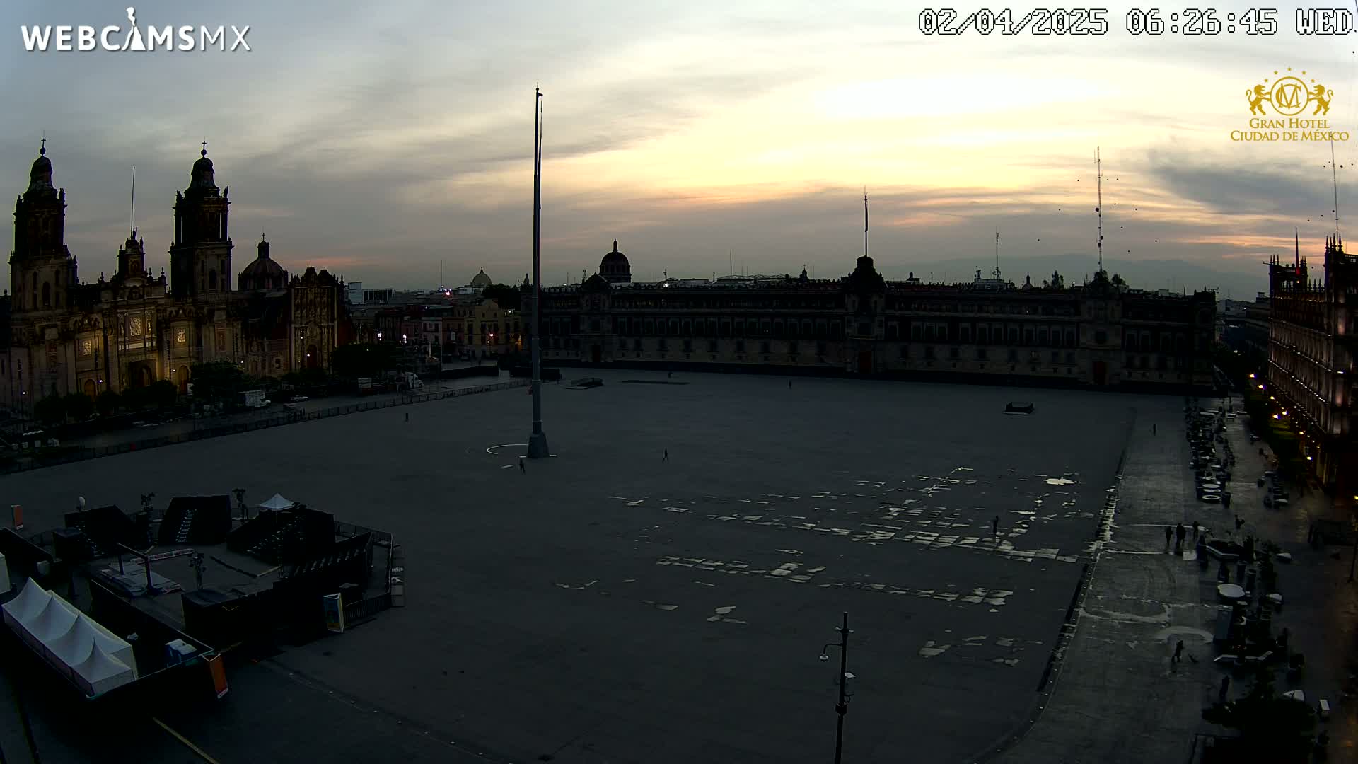 A large, mostly empty plaza at dusk, with a cathedral and a long building visible in the background under a cloudy sky.