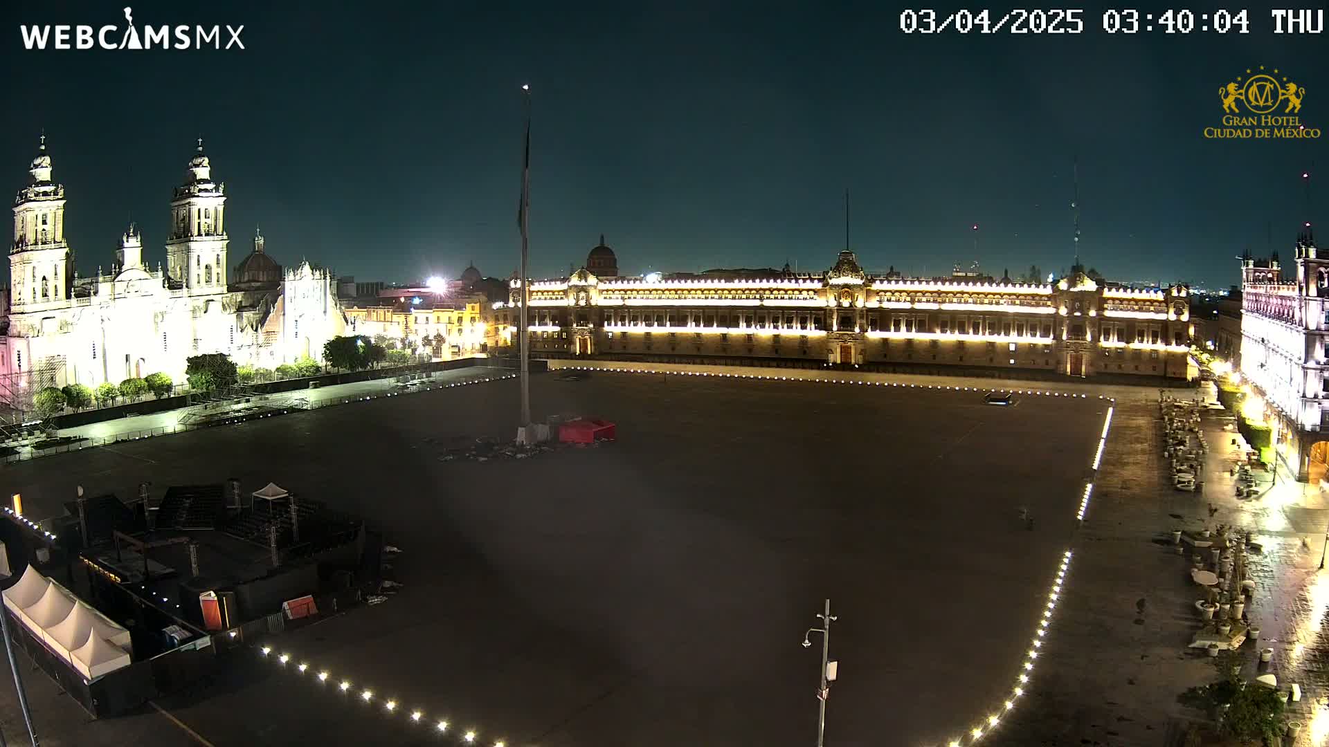 A nighttime, overhead view shows a large, mostly empty plaza with a brightly lit cathedral and palace, under a clear, dark sky.