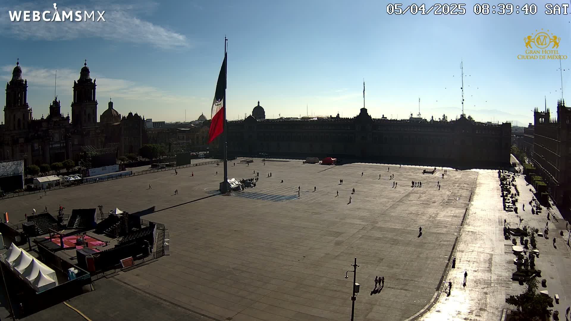 A large plaza in front of a cathedral and government buildings under a clear, sunny sky, with a few people scattered throughout the square and a stage set up for an event.