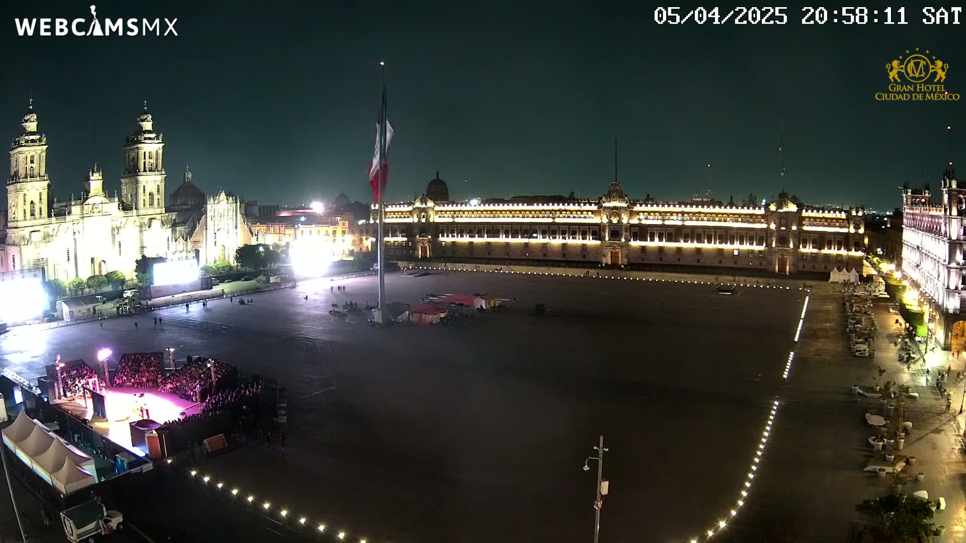 A nighttime aerial view of a large plaza, with a cathedral and government buildings illuminated, under clear skies.
