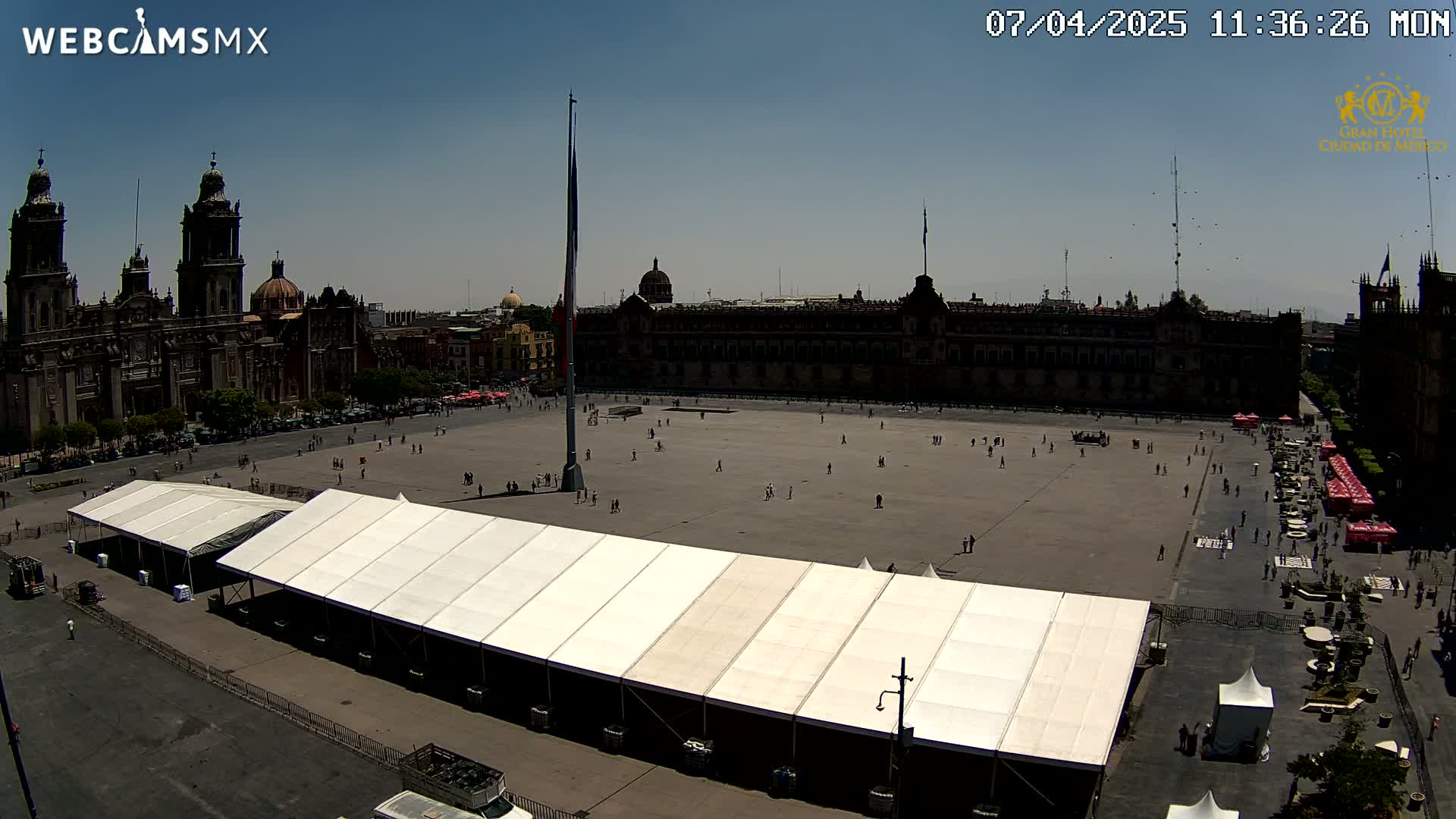 A large plaza with a long white tent, surrounded by historic buildings under a clear, sunny sky.
