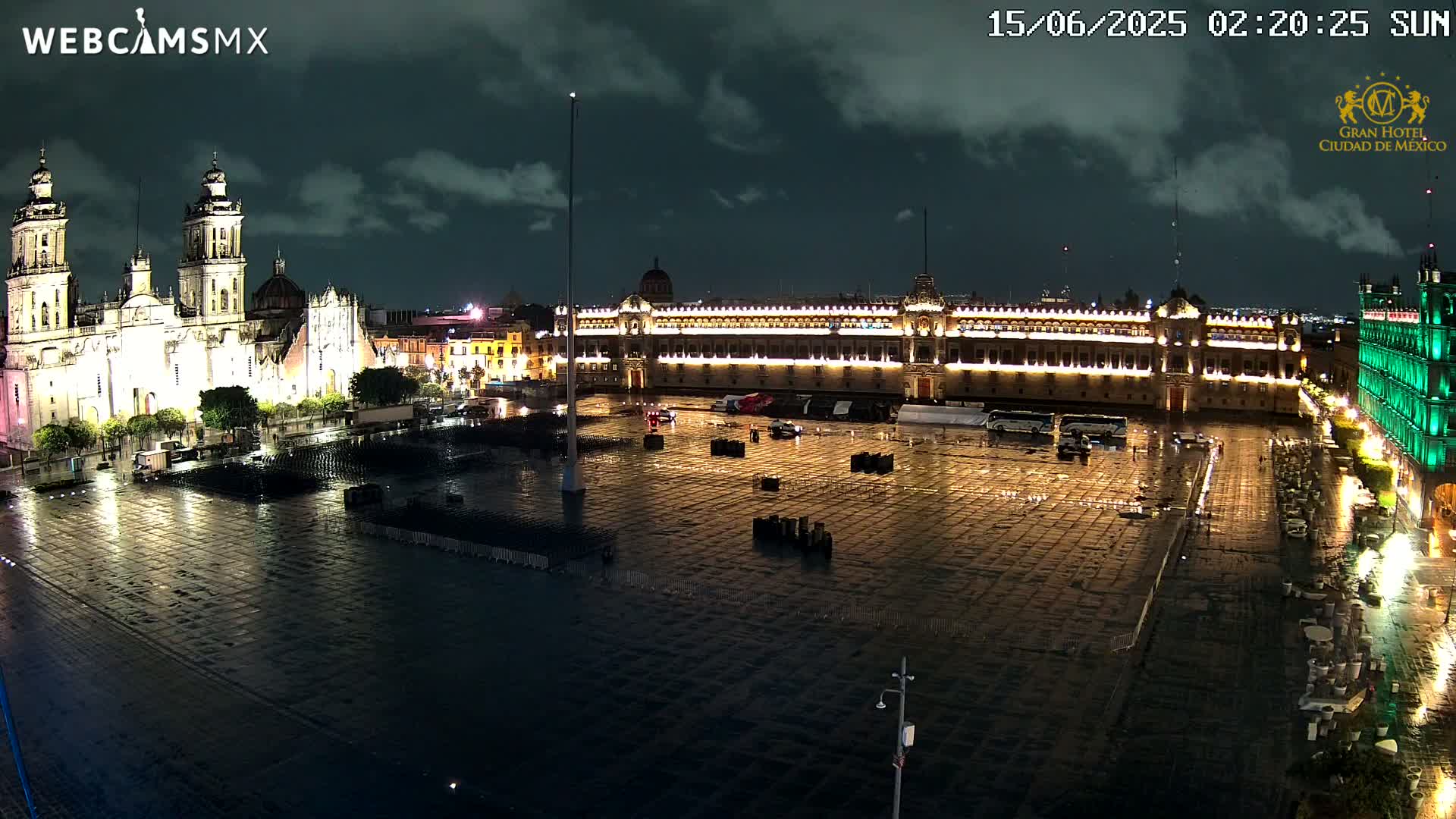 A large, rain-slicked plaza at night, illuminated by the lights of a cathedral and government buildings.
