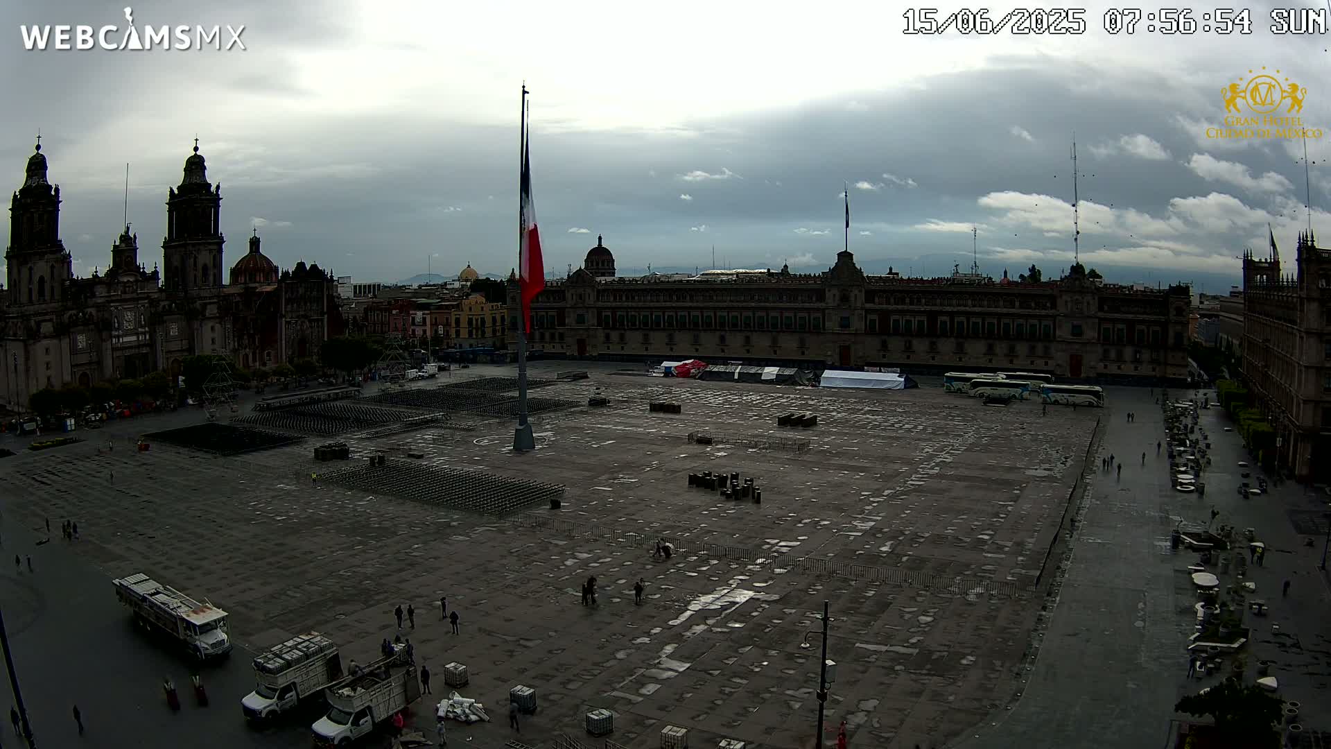 A large plaza with a Mexican flag,  surrounded by historic buildings under a cloudy sky.