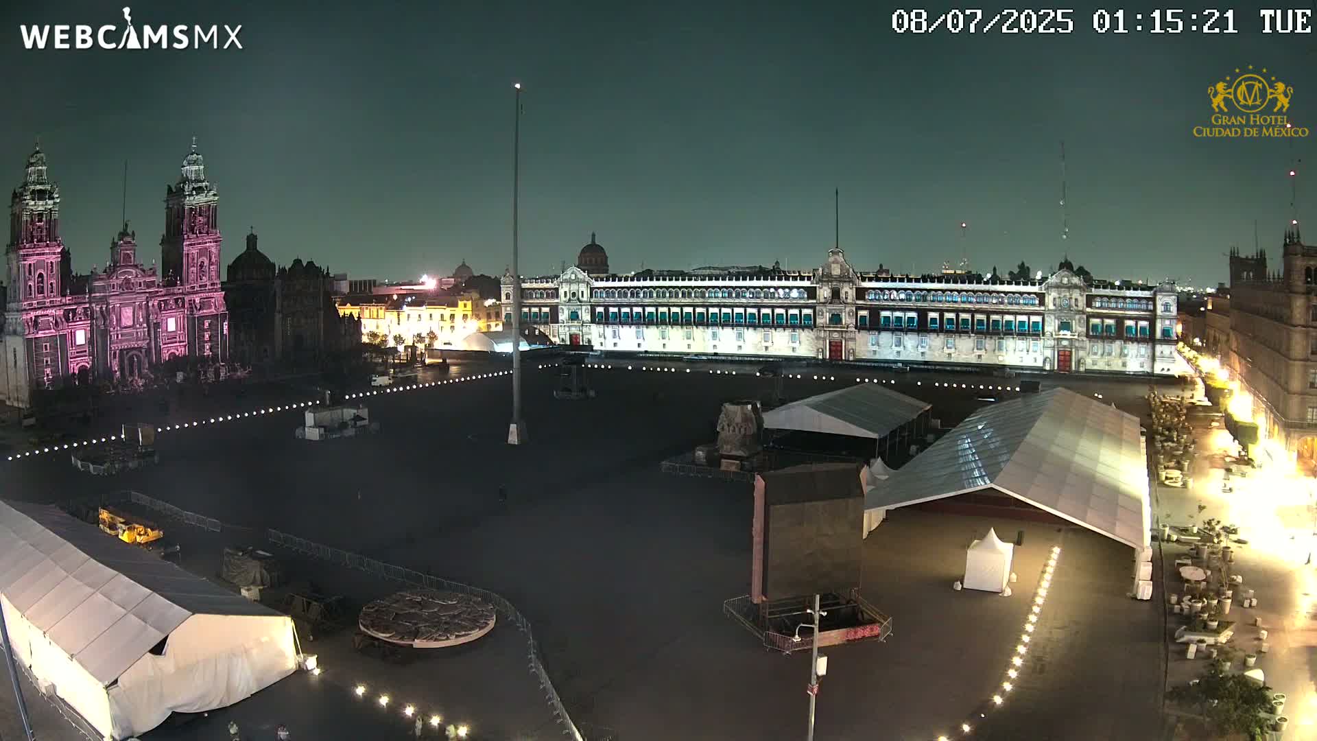A nighttime, high-angle view of a large plaza with a cathedral and palace, surrounded by tents and lights.