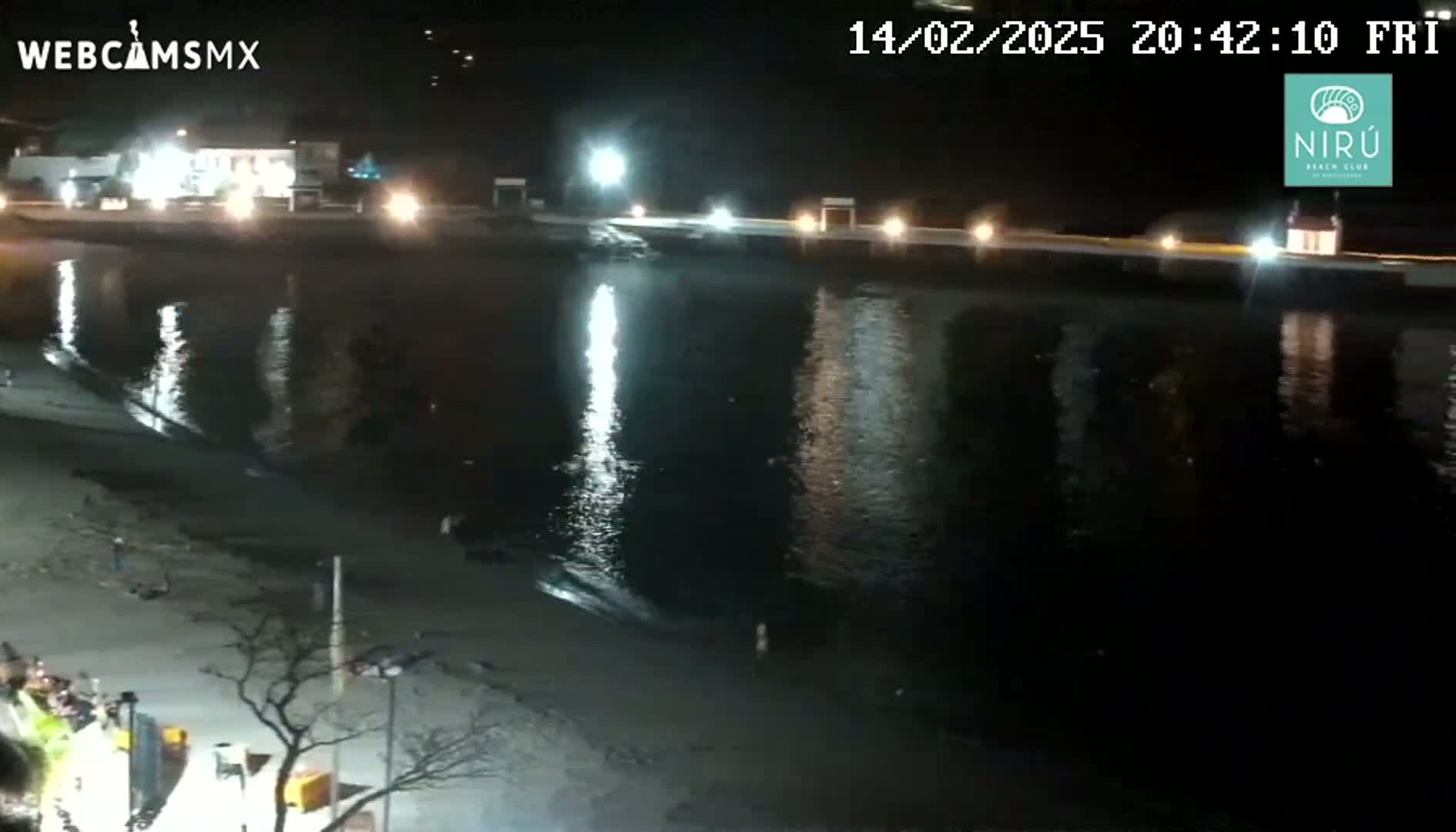 A nighttime view of a calm body of water reflecting lights from a shoreline at night.
