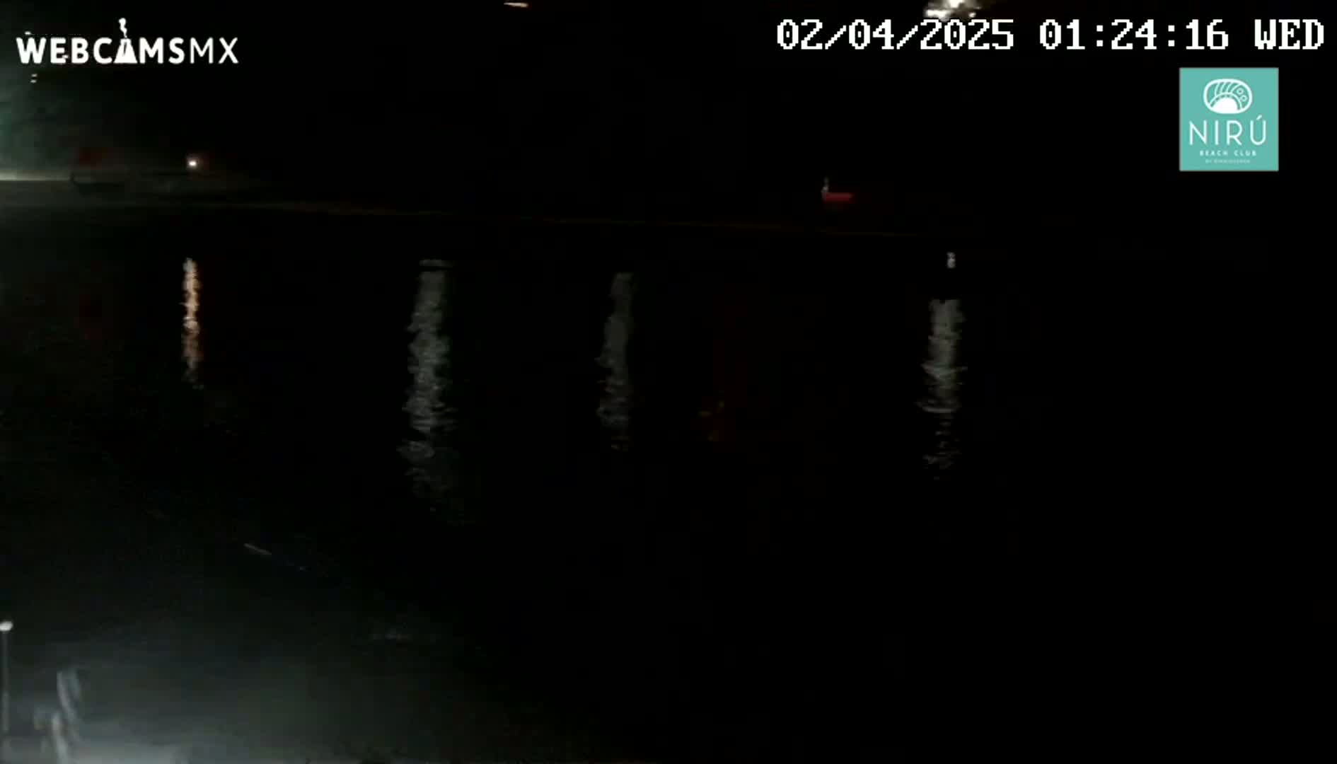 A dark, nighttime view of calm water reflecting faint lights from the shore.