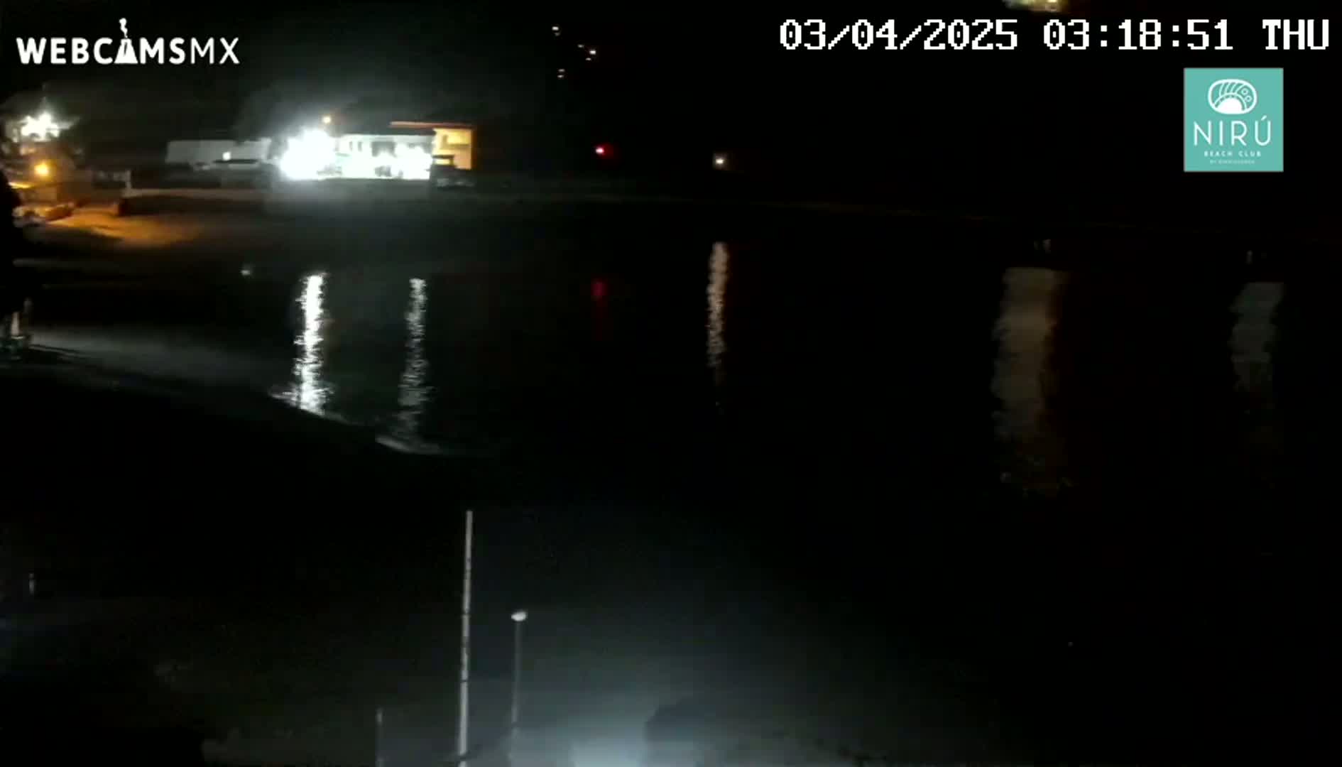 A nighttime view of a dark body of water reflecting lights from a shoreline with buildings and vehicles.