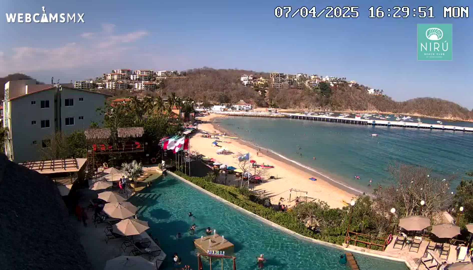 A sunny day overlooking a resort pool and beach with a calm bay and numerous boats in the distance.