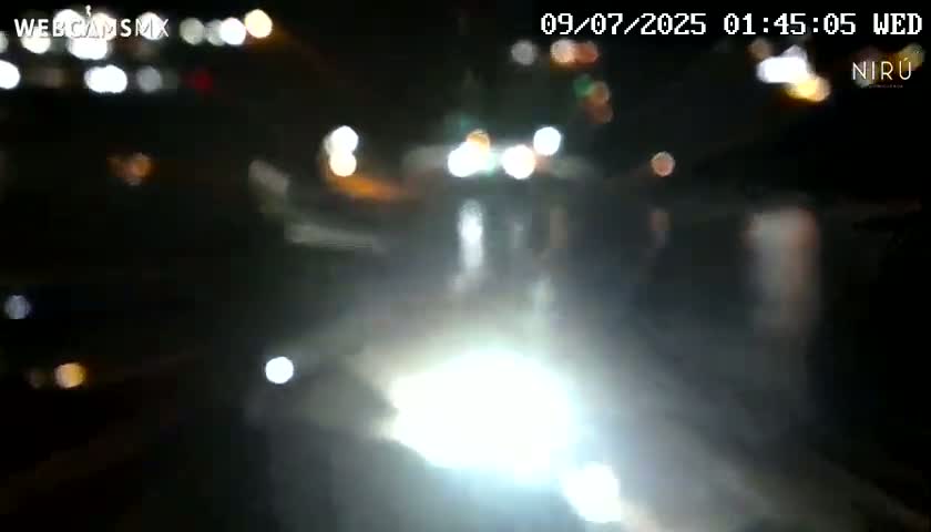 A blurry nighttime view of a road with bright headlights and out-of-focus city lights in the background.