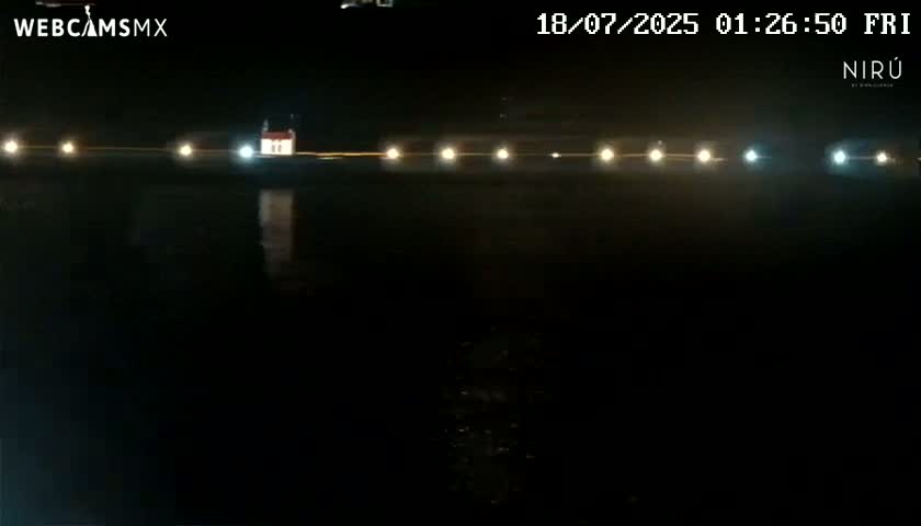 A nighttime view of a dark body of water reflecting lights from a distant structure.
