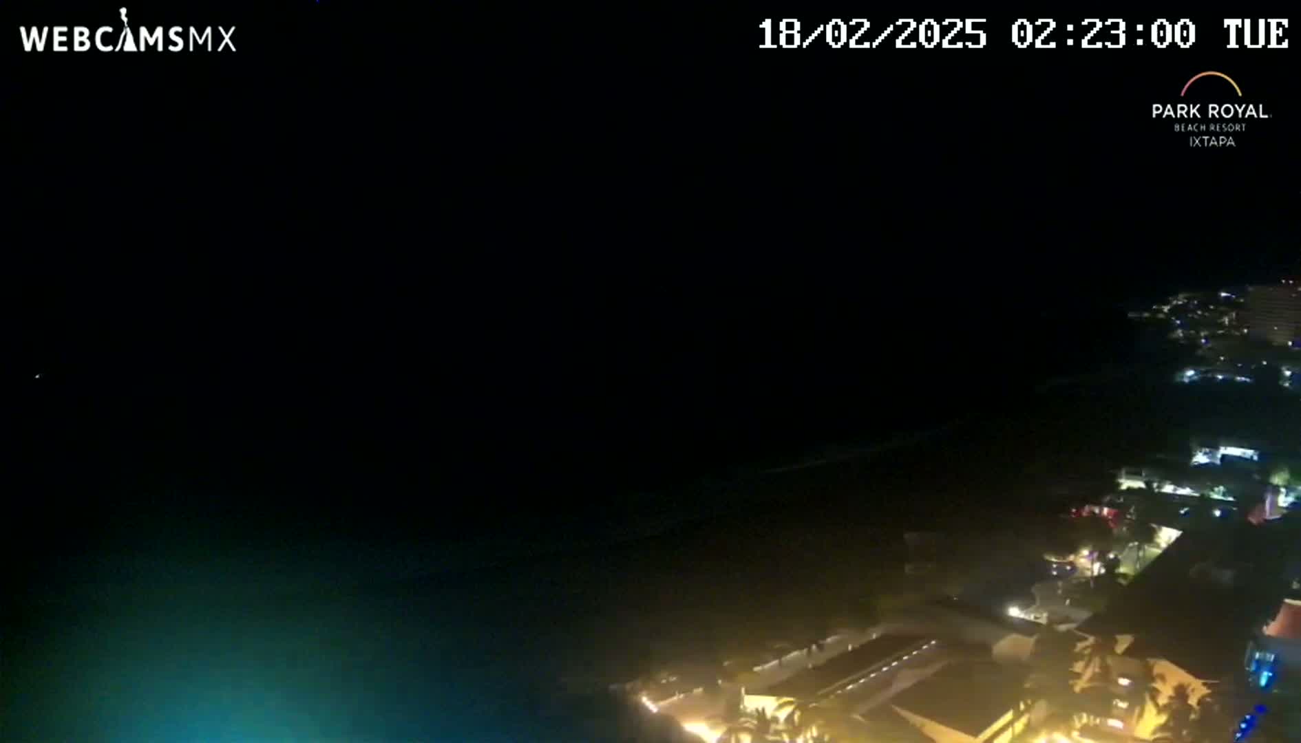 A nighttime, high-angle view shows a dark ocean and a coast with illuminated buildings.