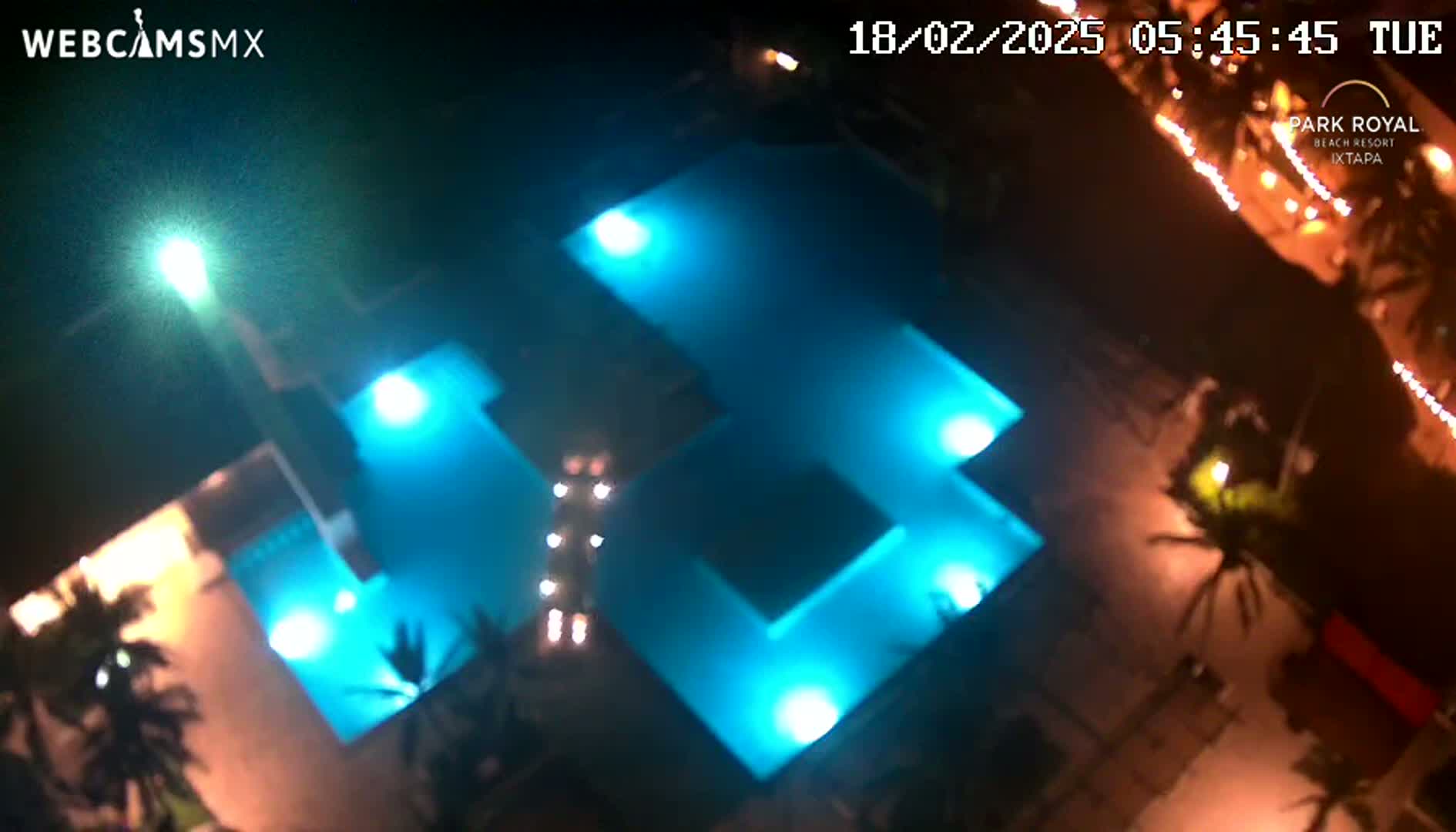 An illuminated, multi-sectioned swimming pool is viewed from above at night.