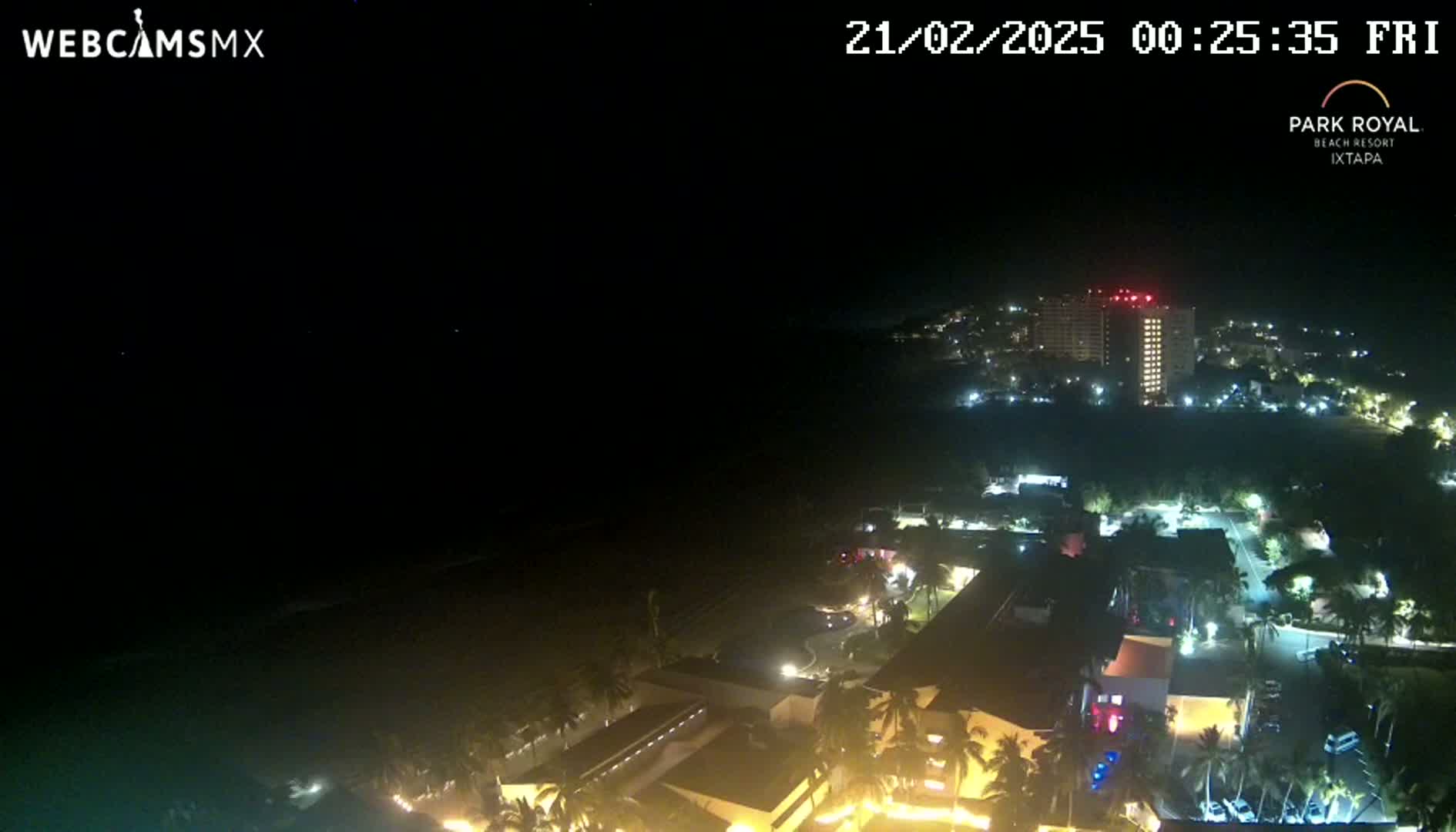 A nighttime aerial view of a coastal resort area, showing lit buildings and palm trees under a clear, dark sky.