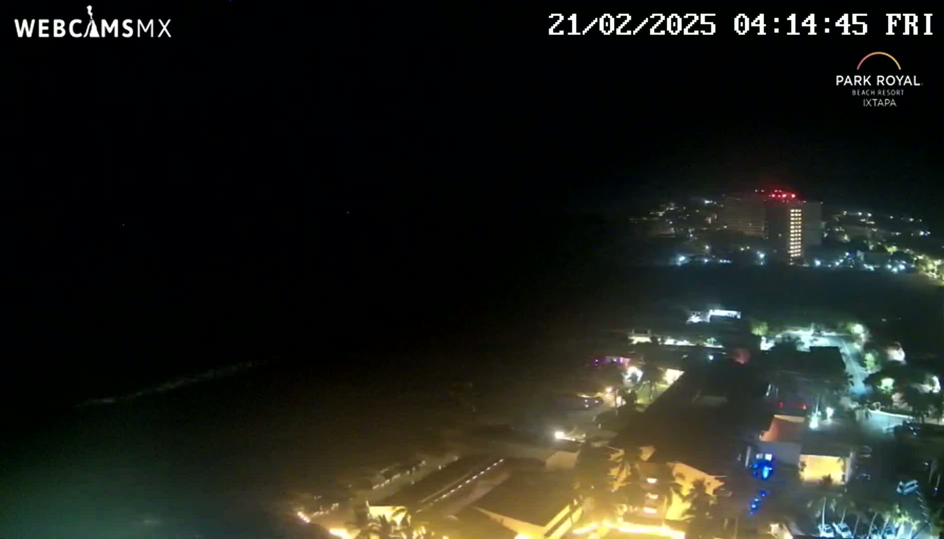 A nighttime, high-angle view of a coastal town with brightly lit buildings and a dark ocean.