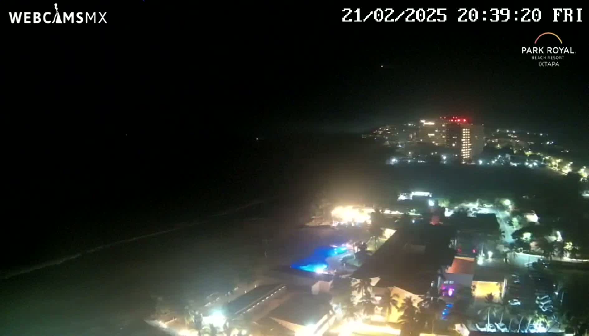A nighttime aerial view shows a coastal resort town with illuminated buildings and a dark ocean under a clear sky.