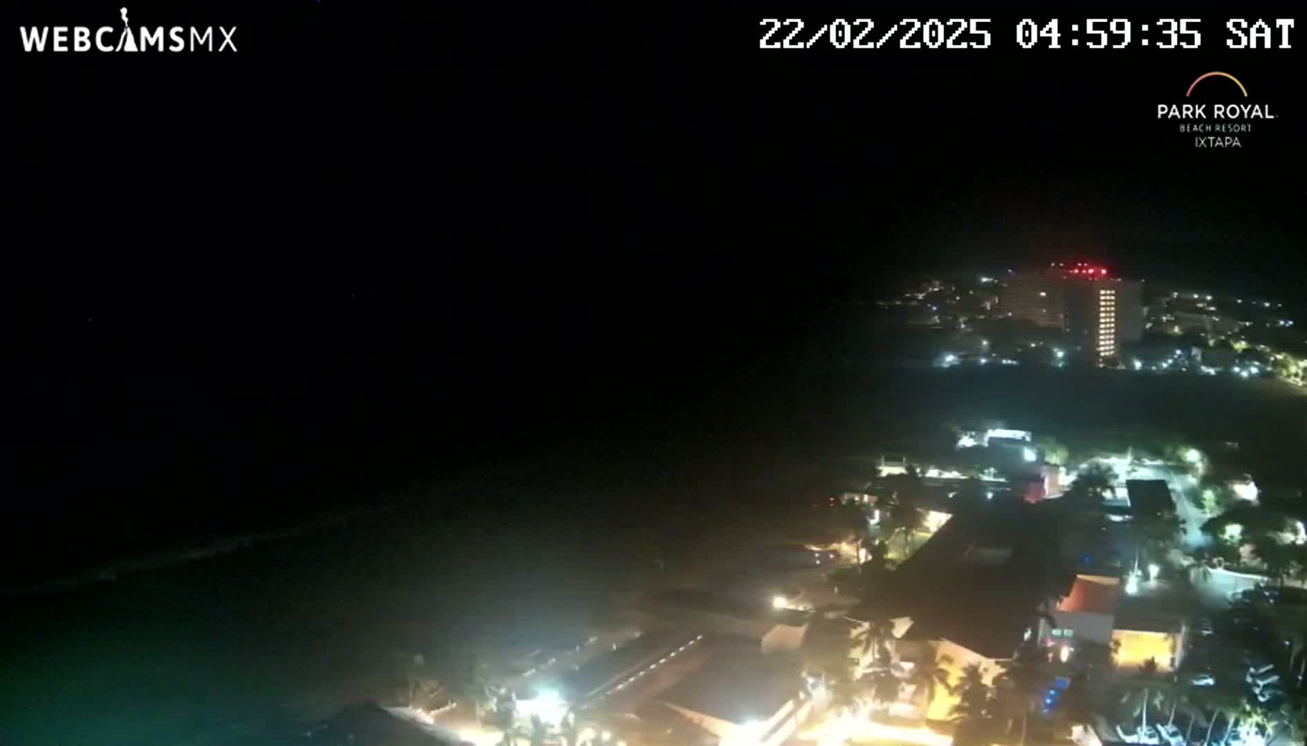 A nighttime, aerial view shows a coastal town with many buildings illuminated, under a clear, dark sky.