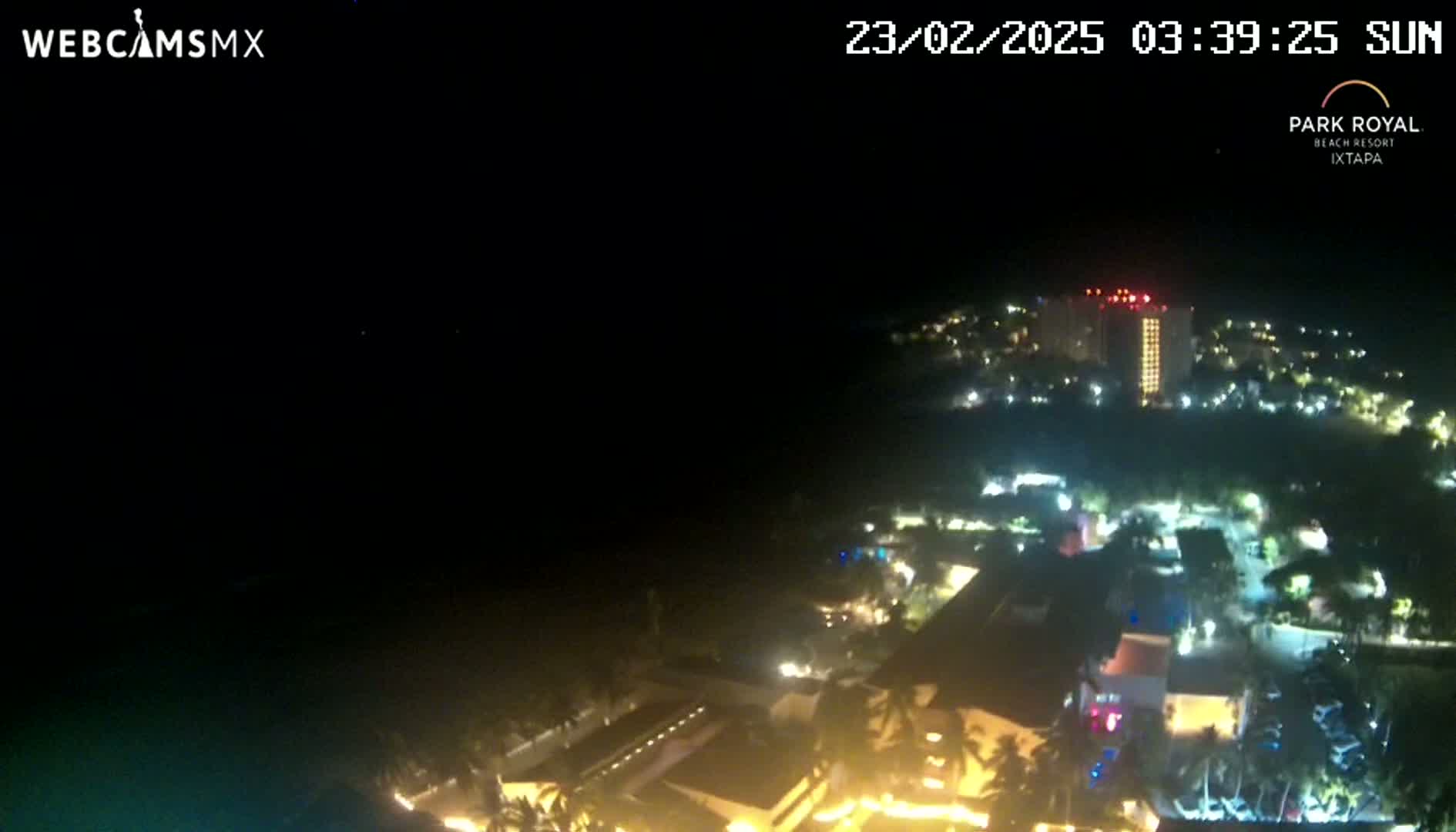 A nighttime aerial view shows a coastal resort town with many buildings illuminated, under a clear, dark sky.