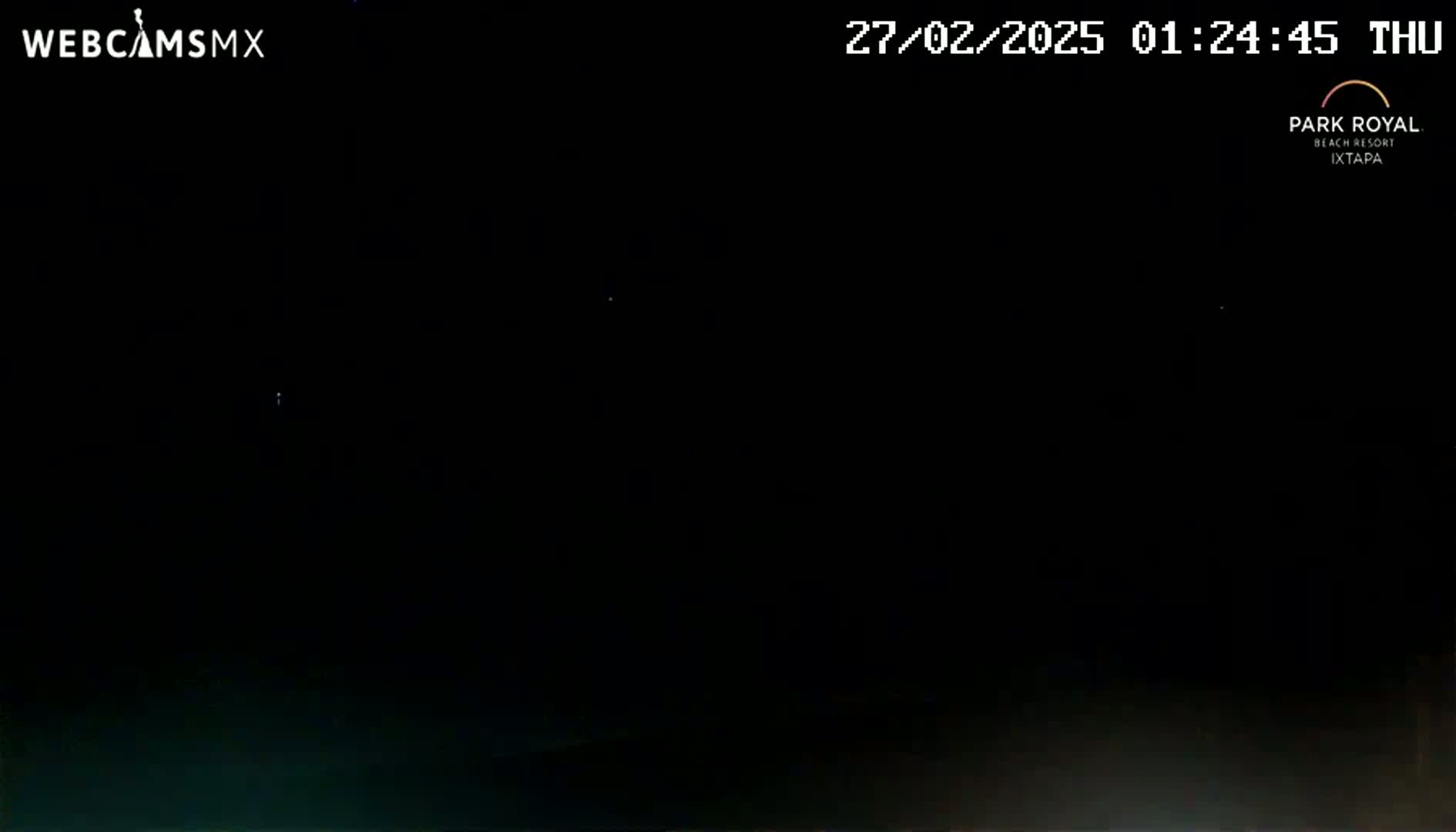 A nighttime image shows a dark, mostly black scene with a few faint lights visible in the distance.