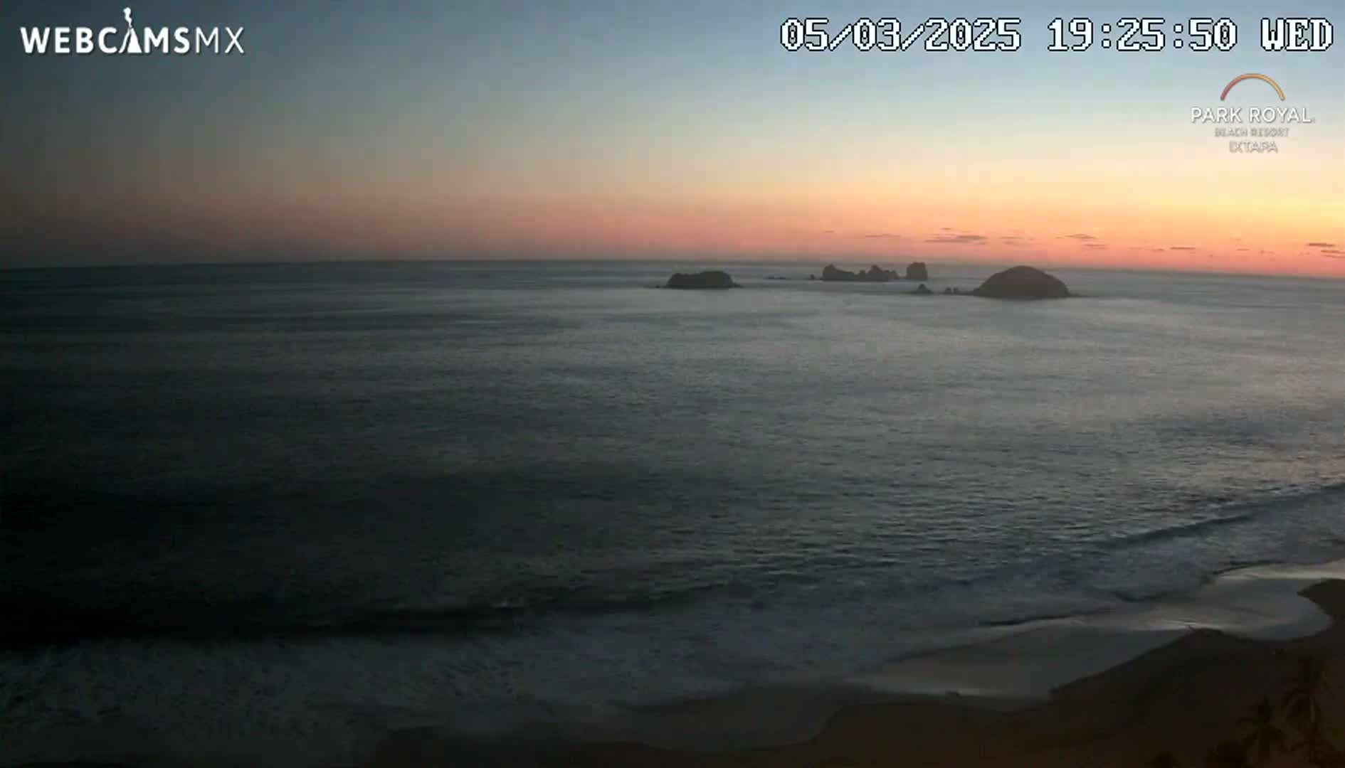 A twilight ocean scene shows dark water lapping a sandy beach under a pinkish-orange sky.