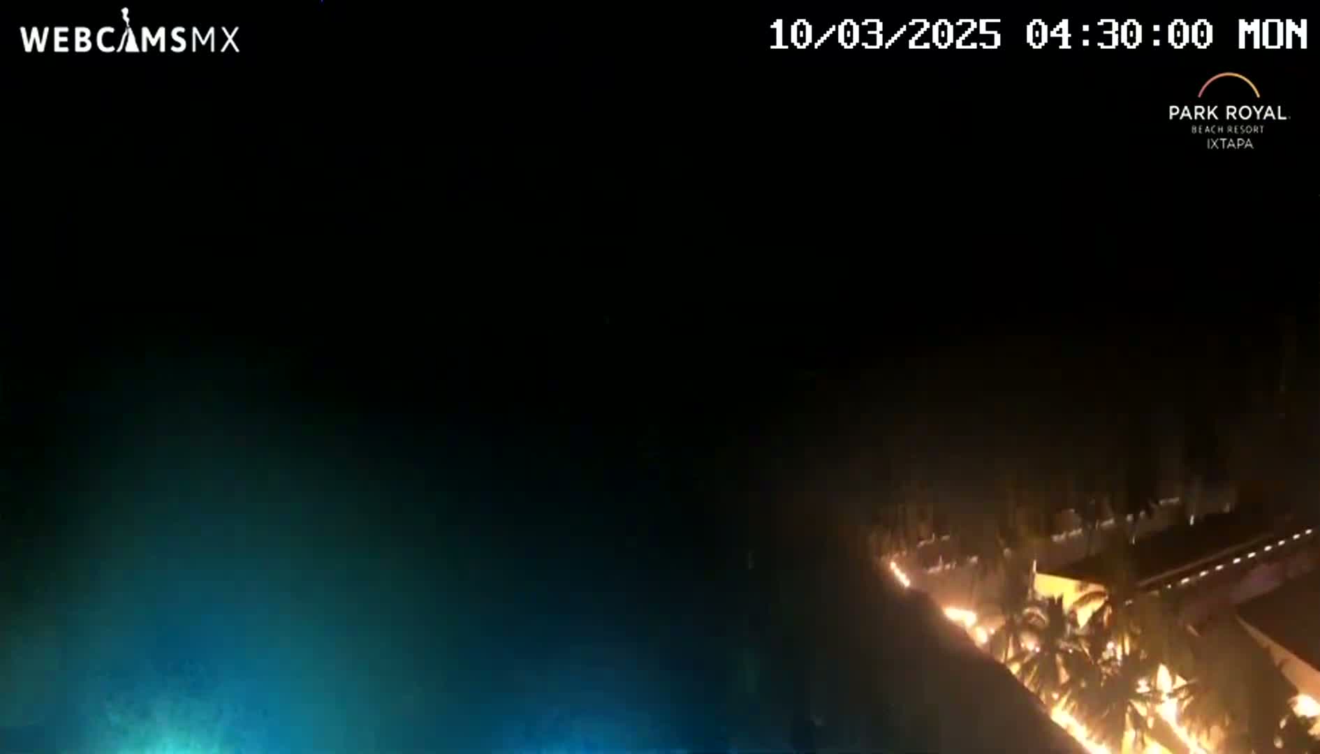 A nighttime, high-angle view shows a resort area illuminated with lights, situated near a dark body of water.