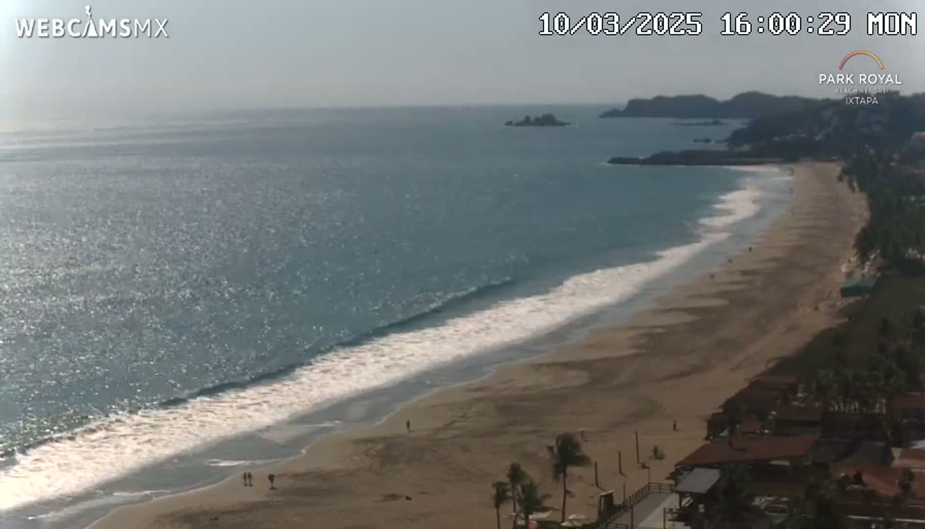A sandy beach with gentle waves laps the shore under a bright, sunny sky.
