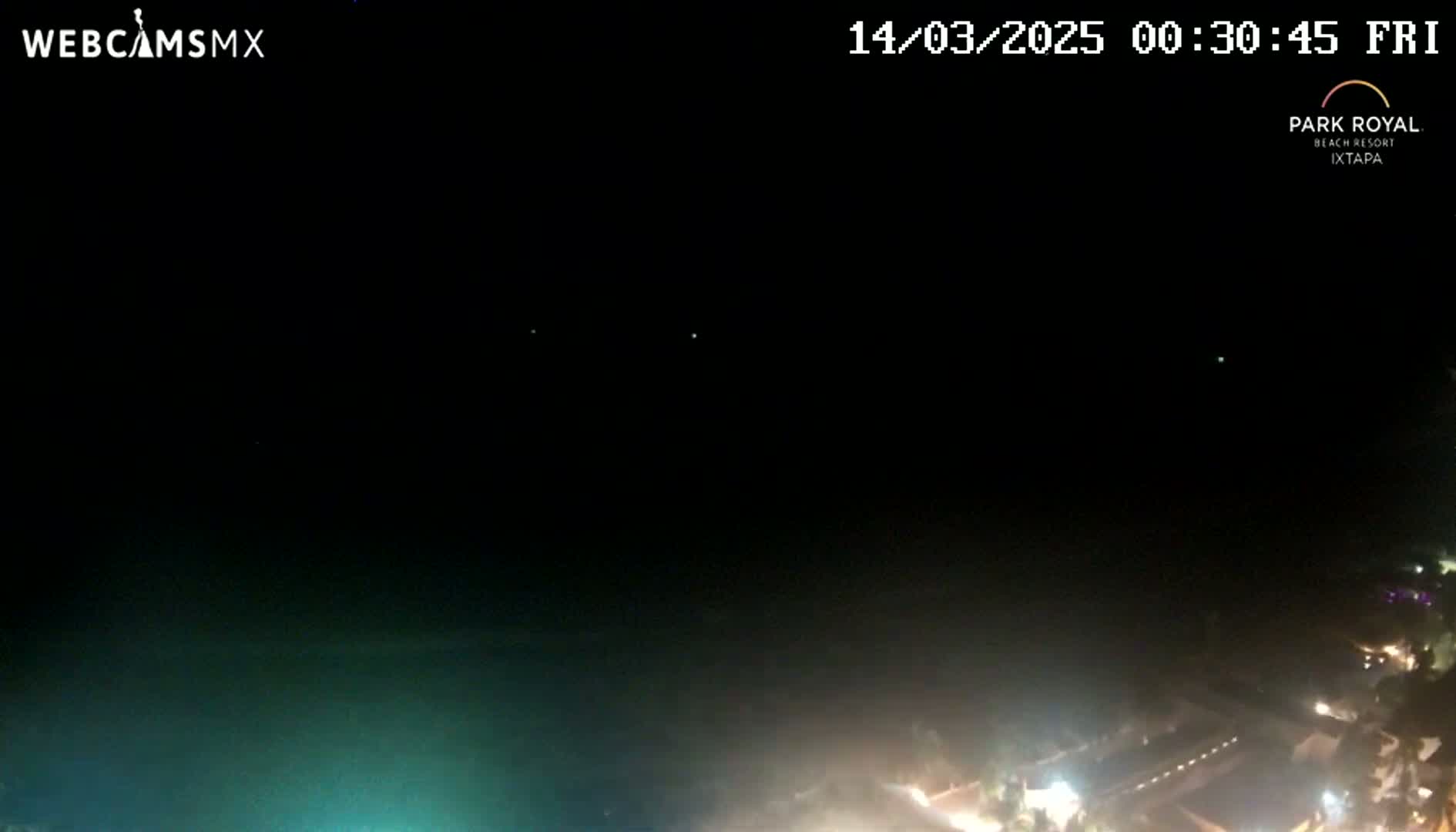 A nighttime, aerial view shows a dark body of water with faintly illuminated areas of land and a few distant lights.