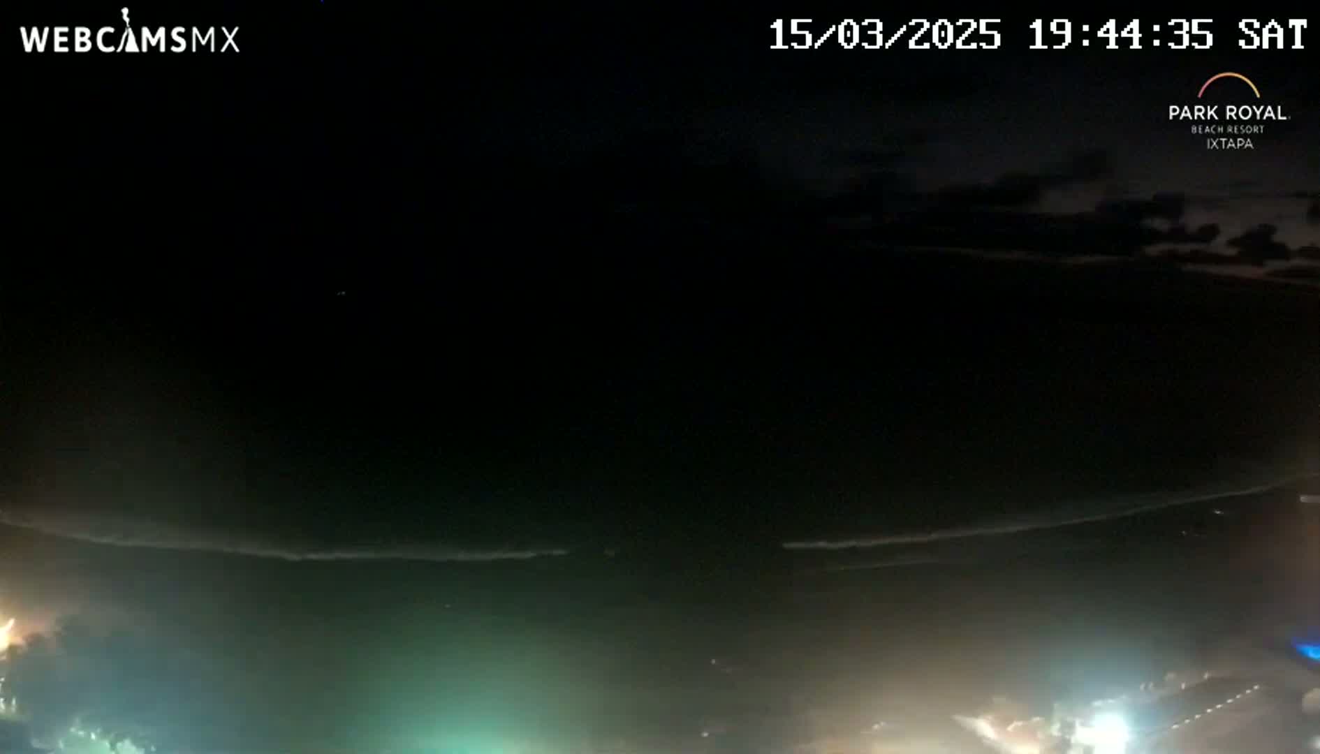 A nighttime, high-angle view shows a dark ocean with faint waves and a shoreline with scattered lights.