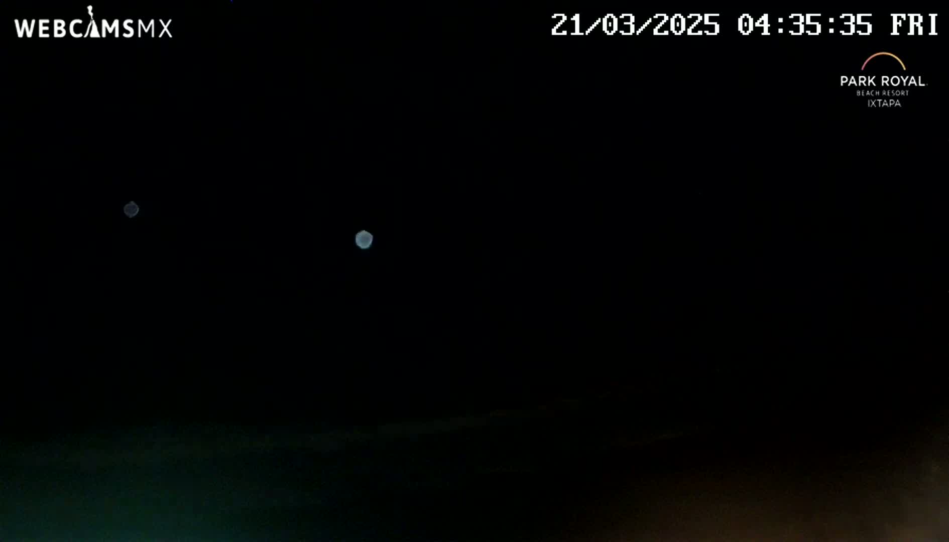 A nighttime outdoor image shows two blurry, bright lights in the dark sky above a dark, indistinct horizon.